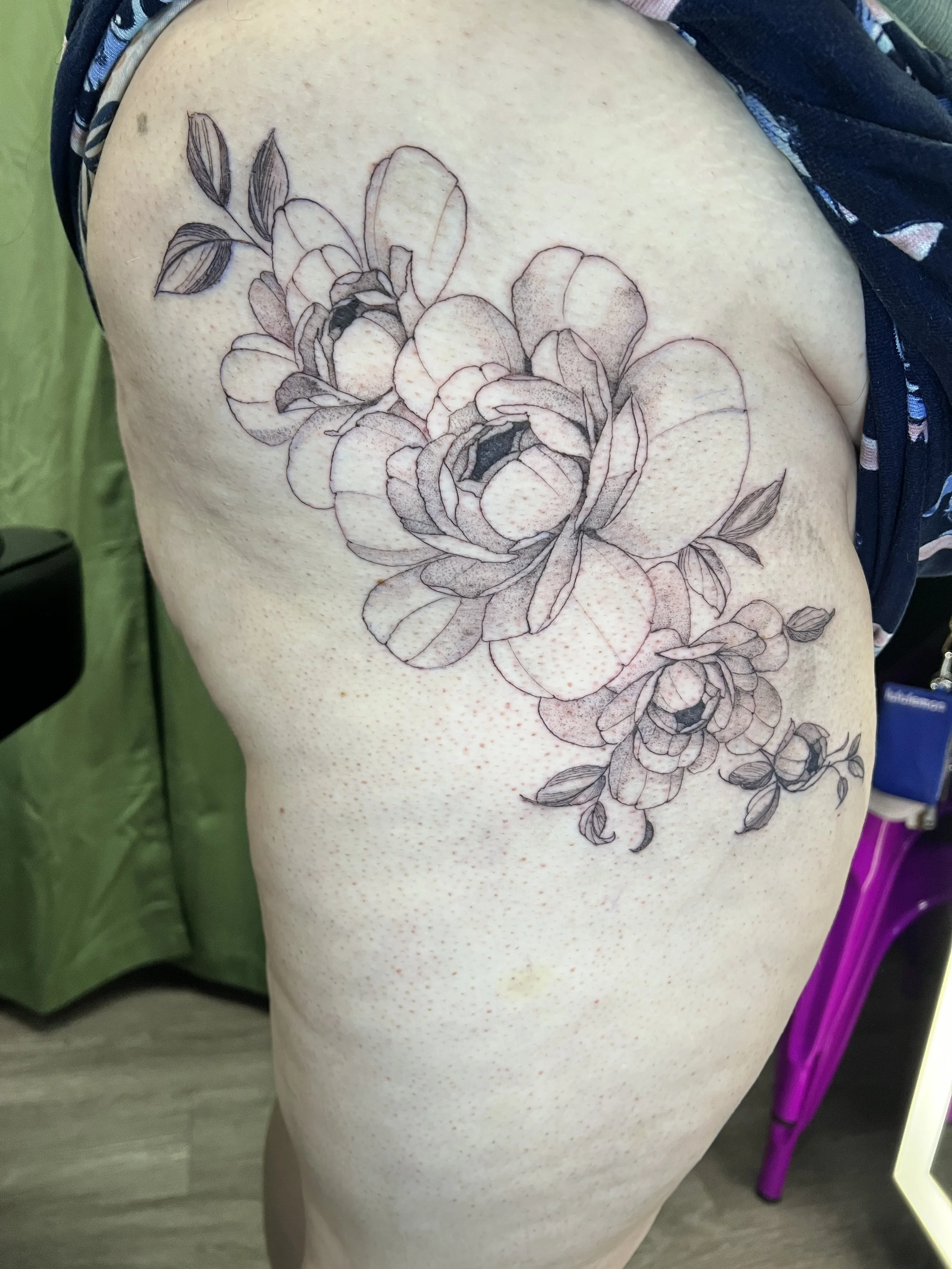 A person's shoulder and upper arm with a floral tattoo fine line of large roses and leaves.