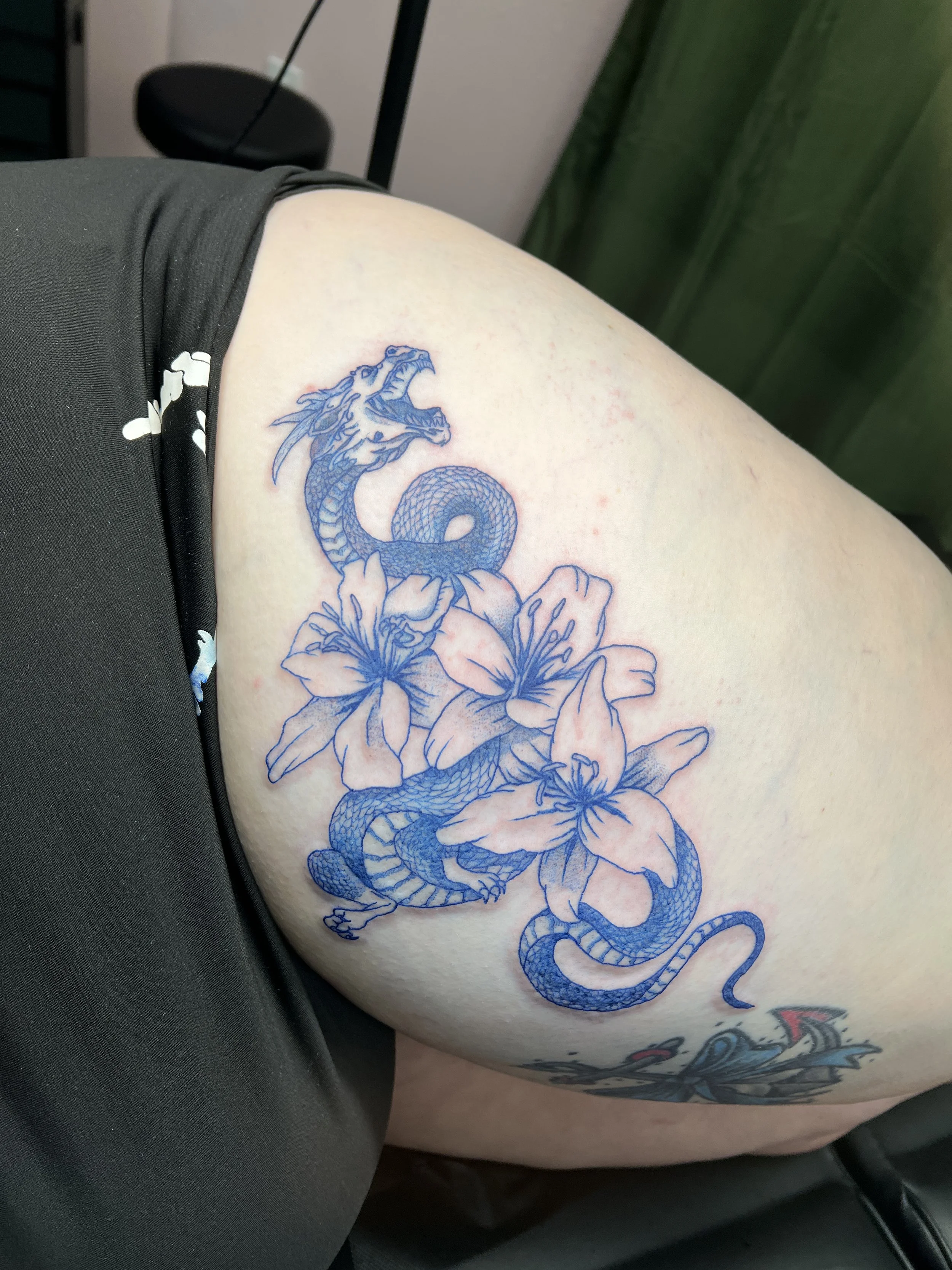 Tattoo of a blue dragon intertwined with flowers on a person's upper arm.