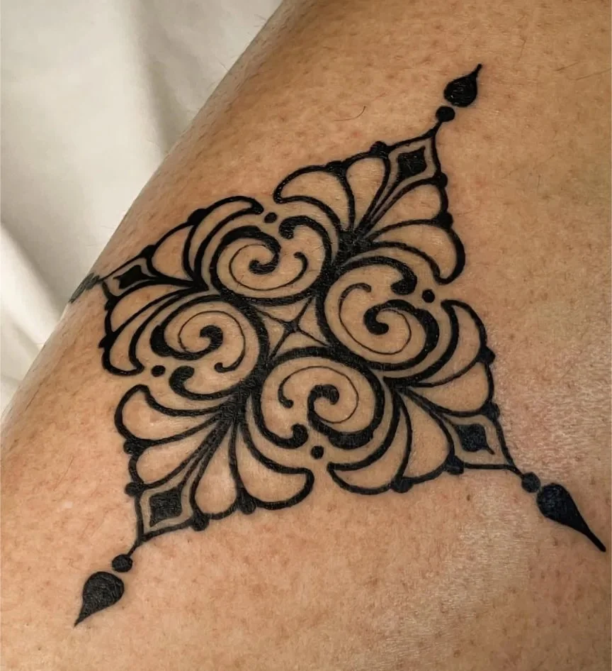 Black ornate butterfly tattoo on skin with intricate swirl and diamond patterns.