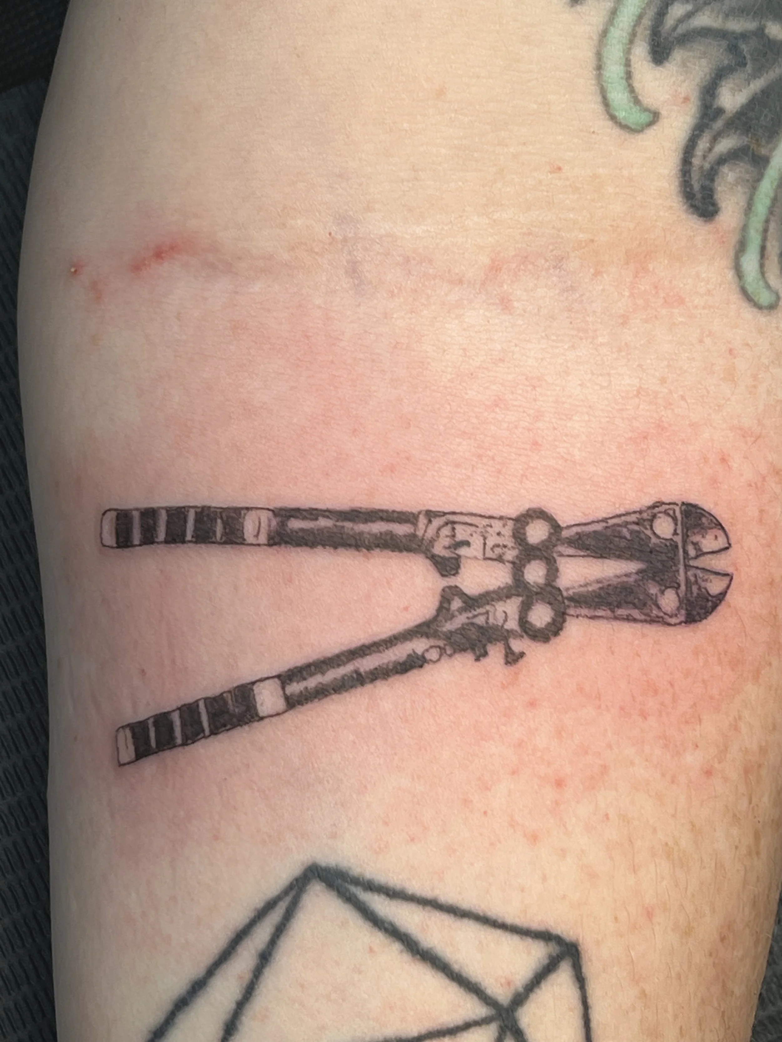 Close-up of a tattoo on skin featuring a design of knives or swords and a cannabis leaf.