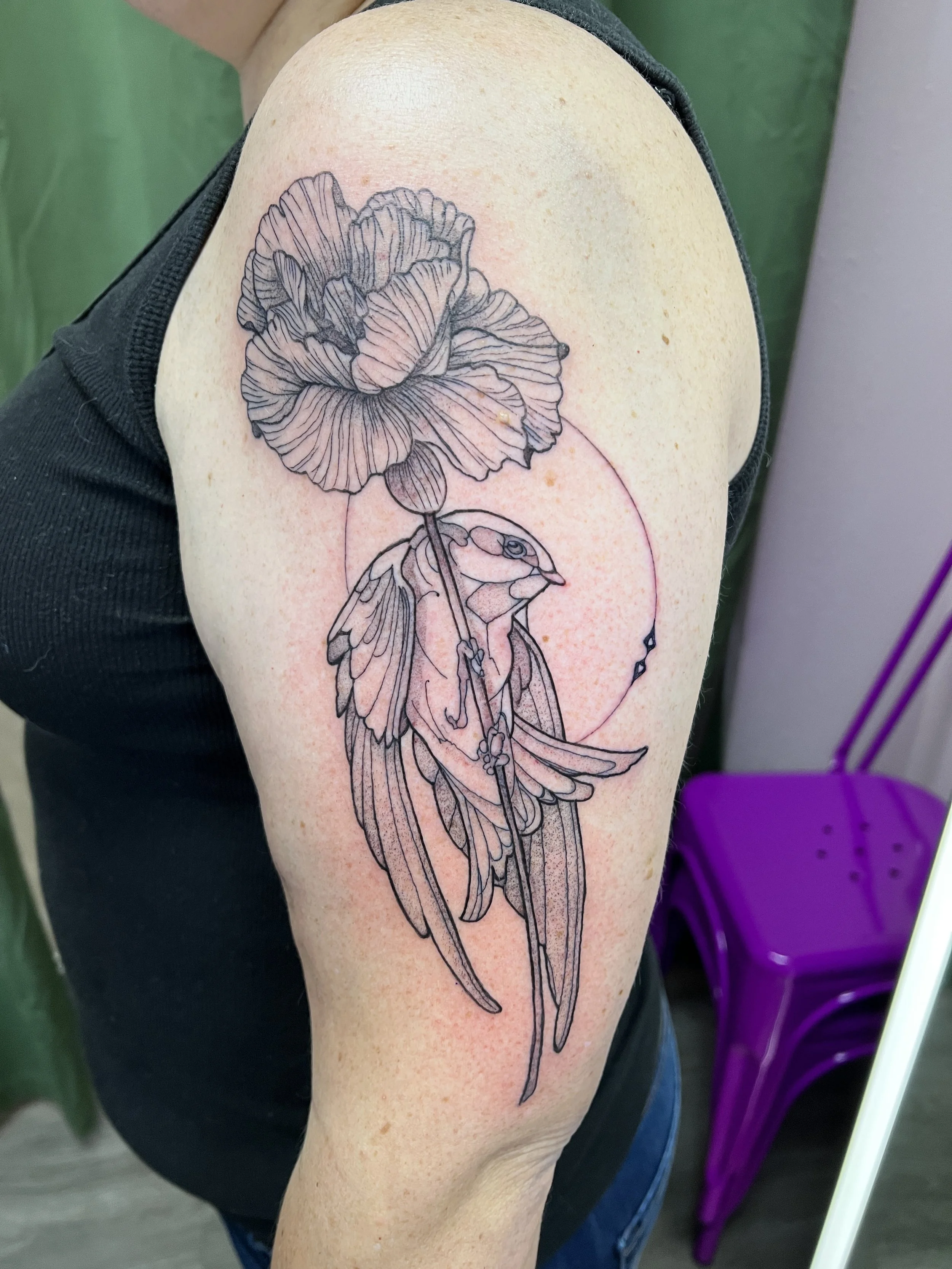 A tattoo of a large flower with detailed lines on a person's upper arm.