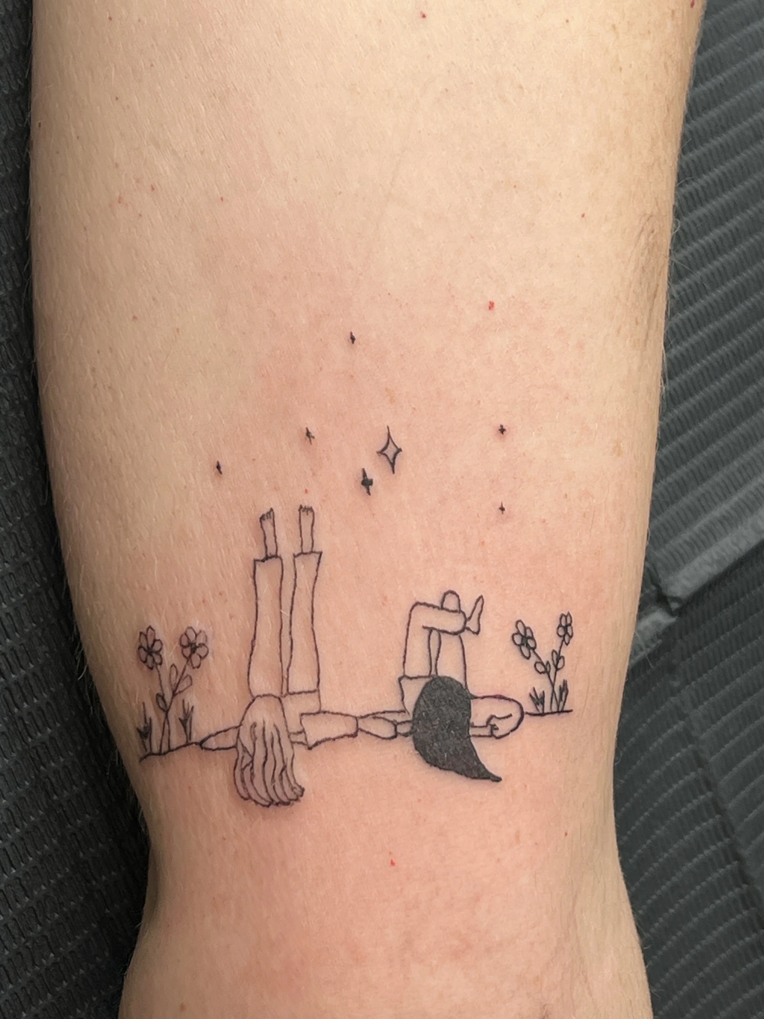 Tattoo of a girl lying on her stomach with her haircut and skirt visible, surrounded by flowers and stars.