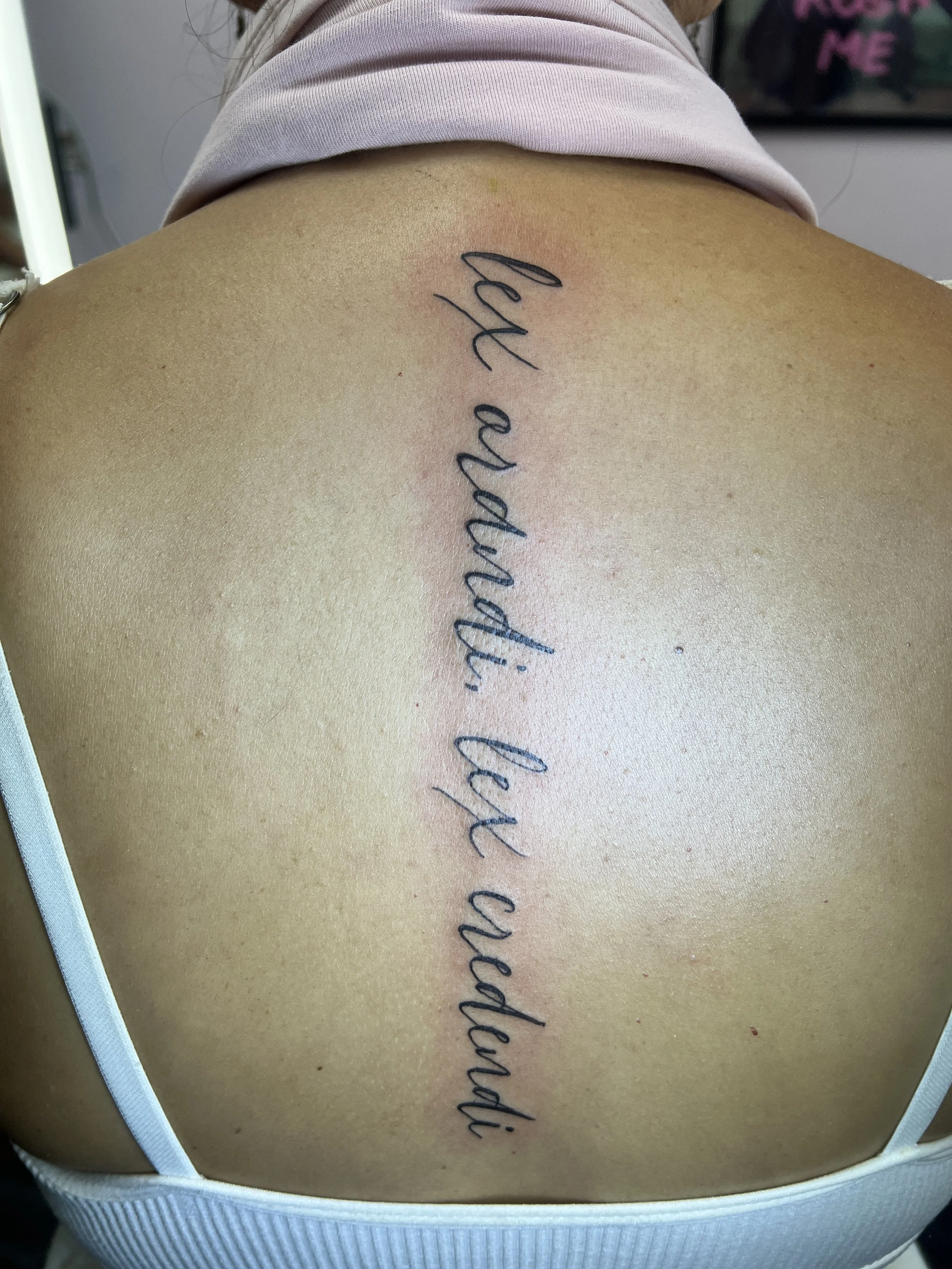 Close-up of a person's upper back and shoulder, showing a tattoo with cursive text under the skin's surface near the shoulder blade.