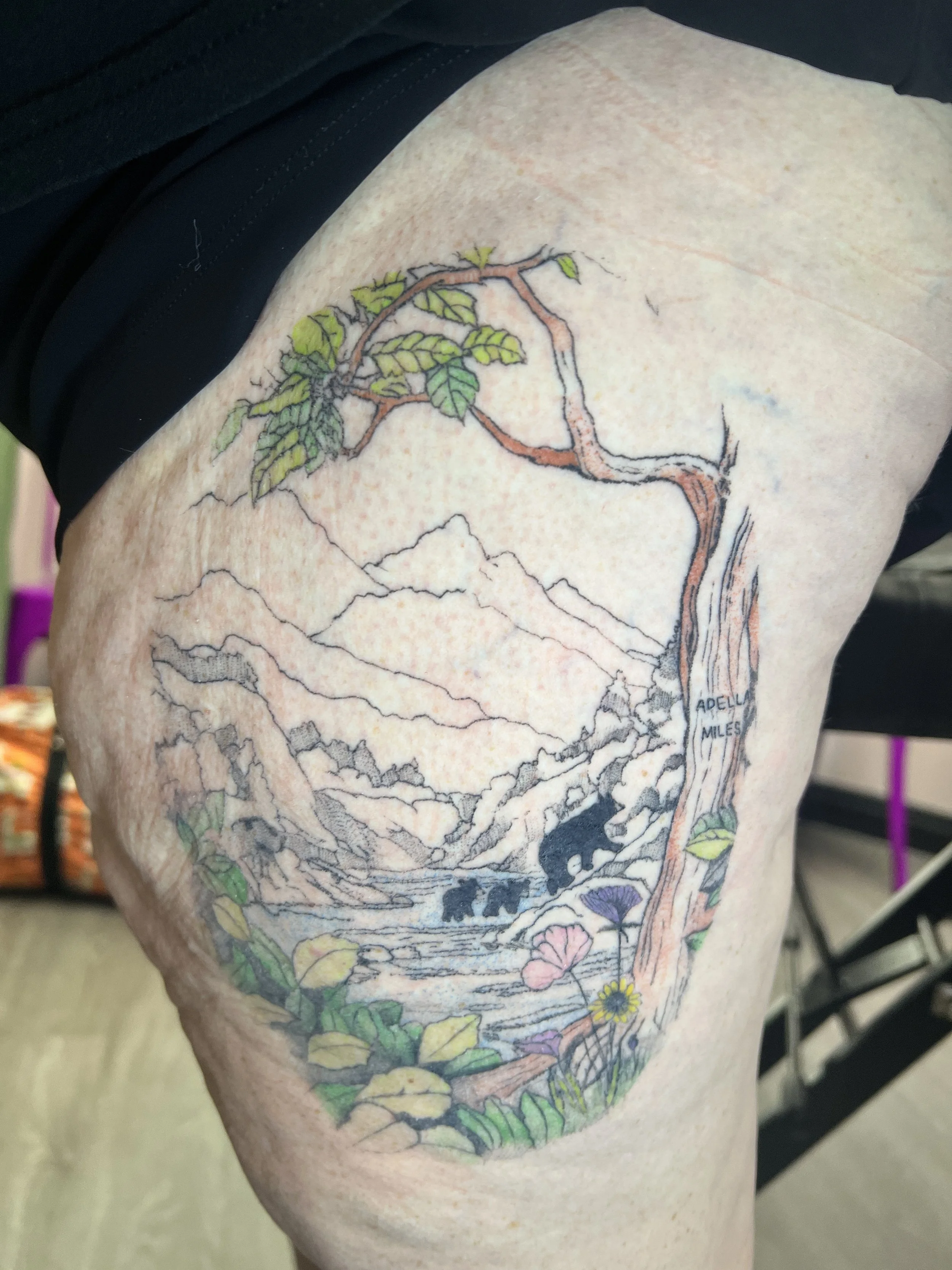 Colorful fine line tattoo of a tree with leaves, flowers, and roots on person's arm.