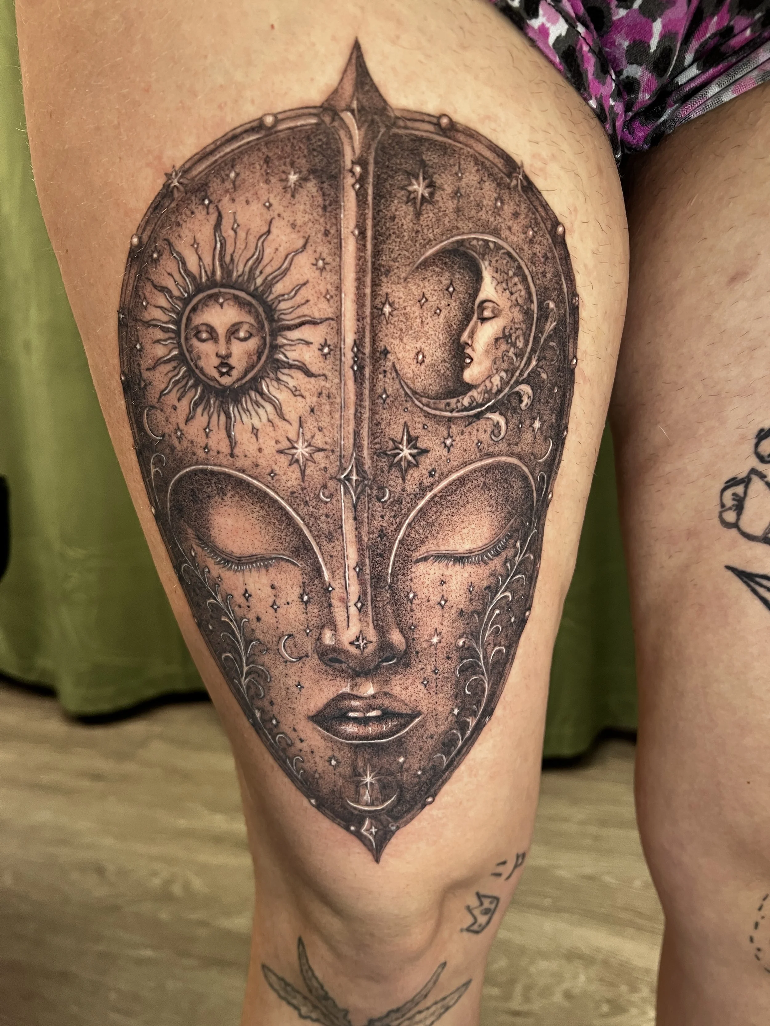 Tattoo of a woman's face with the sun and moon surrounding her, celestial elements, stars, and decorative accents on arm.