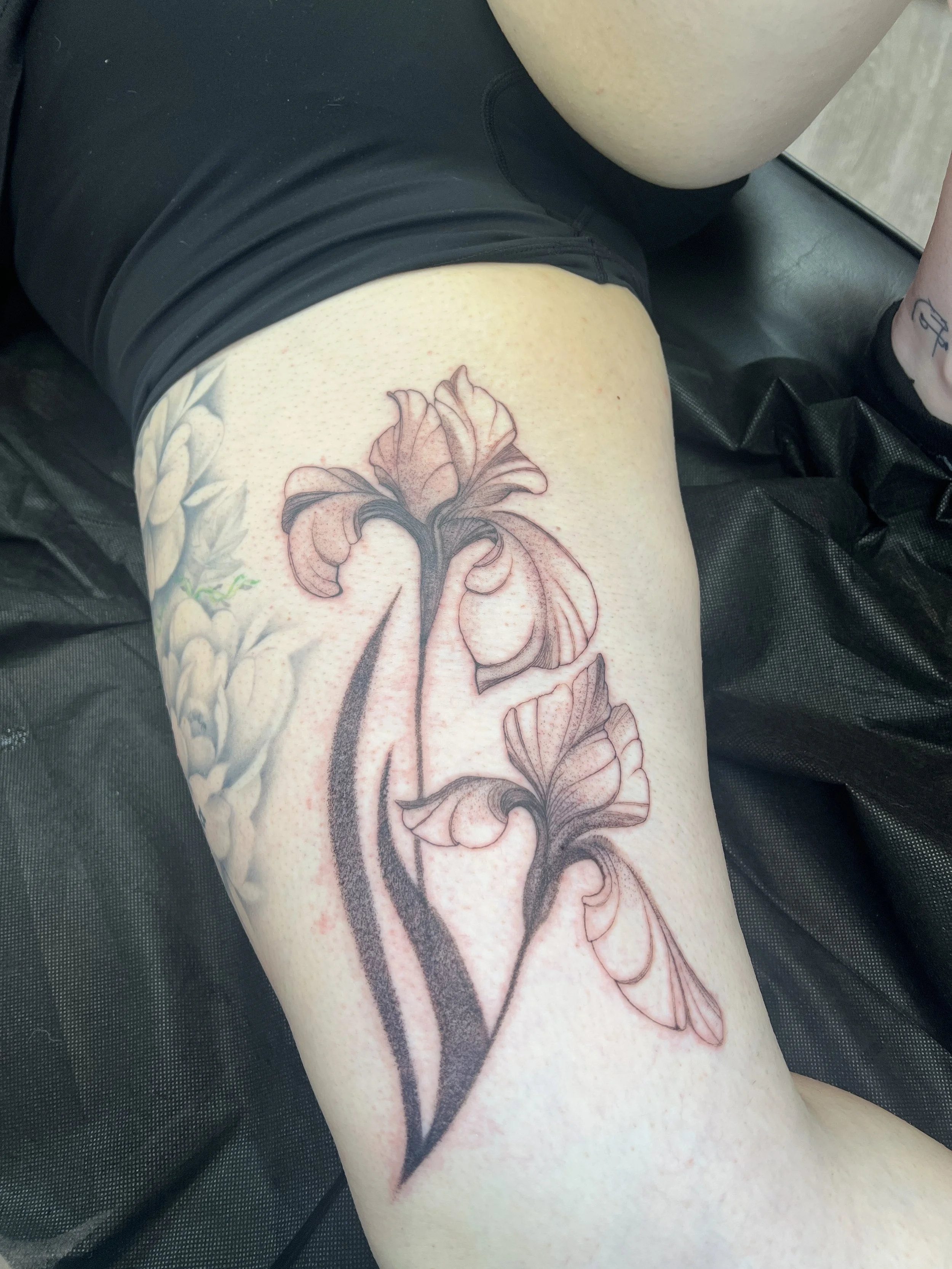 Close-up view of a person's thigh with a detailed floral tattoo design featuring flowers and leaves.