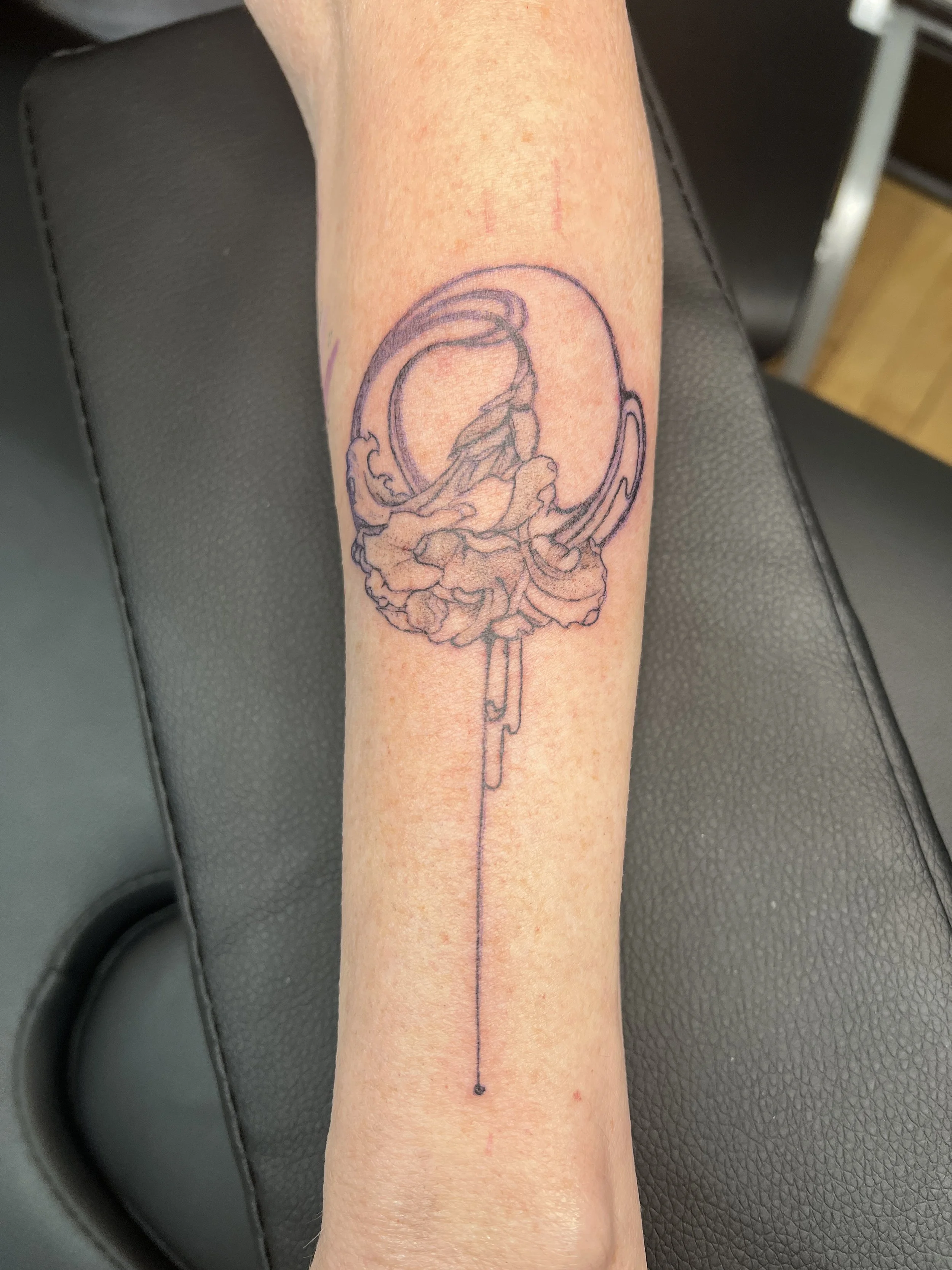 A person's forearm with a tattoo outline of a dragon and a circle, with a dotted line extending downward.