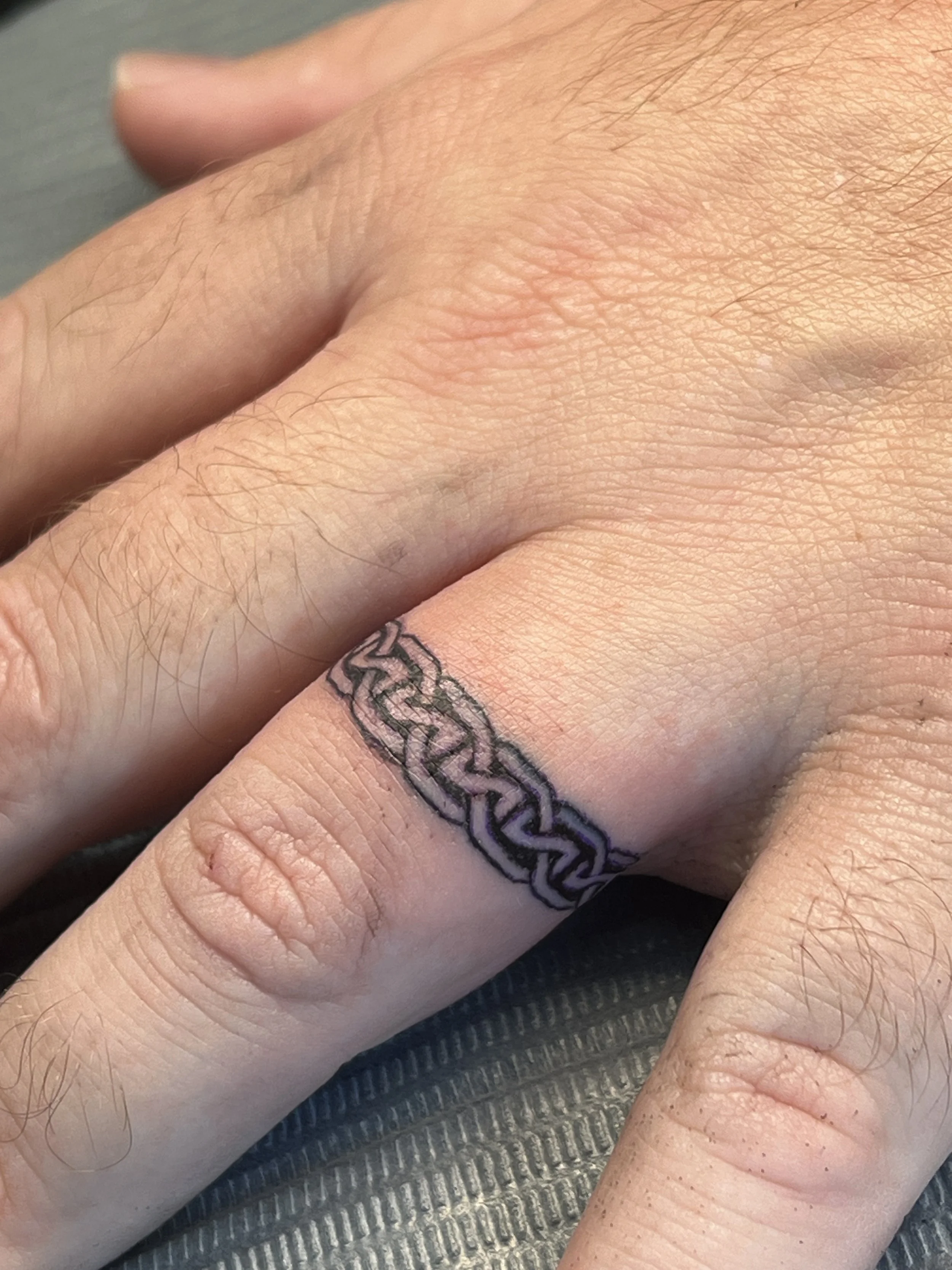 Close-up of a hand with a Celtic knot tattoo on the finger.