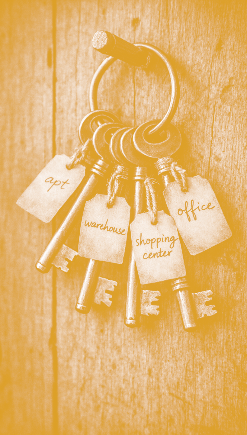 Set of vintage keys hanging on a hook on a wooden wall, each with a paper tag labeled 'apt', 'warehouse', 'shopping center', and 'office'.
