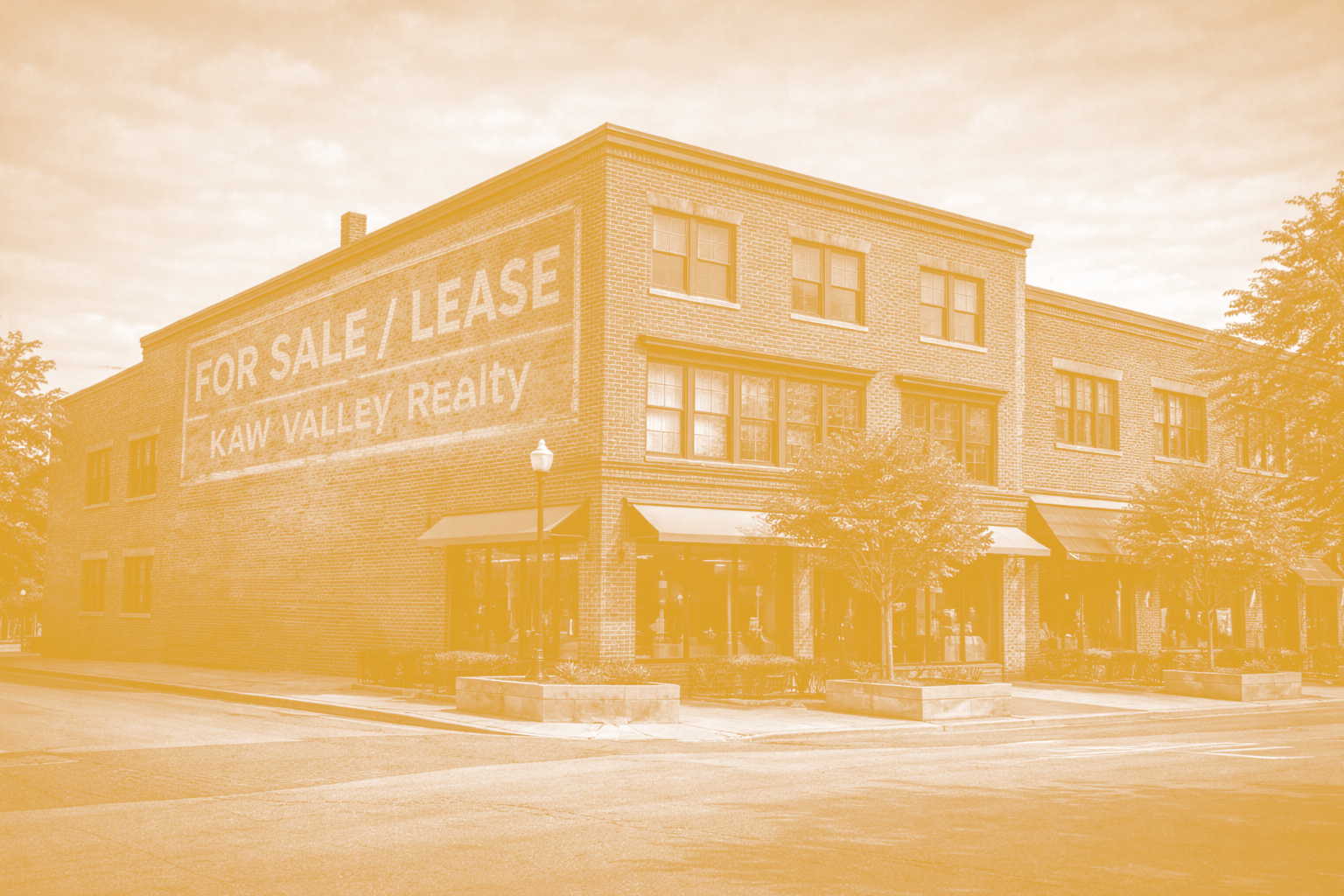 A brick building with a large sign on the side that reads 'For Sale / Lease, Kaw Valley Realty'. The building has multiple windows, some with awnings, and a sidewalk with small trees and benches in front.