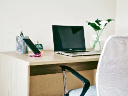 A tidy desk with a laptop, a mug, and stationery, alongside a potted plant and a white chair.
