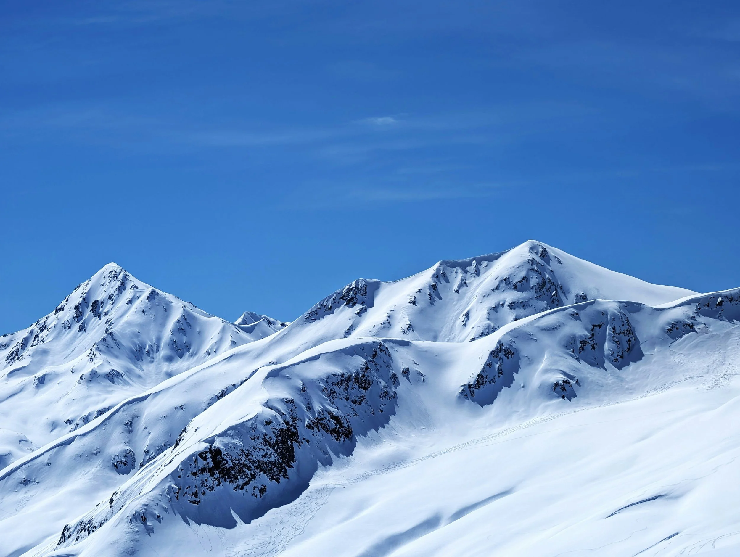Snow-covered mountain peaks under a bright blue sky with some wispy clouds.