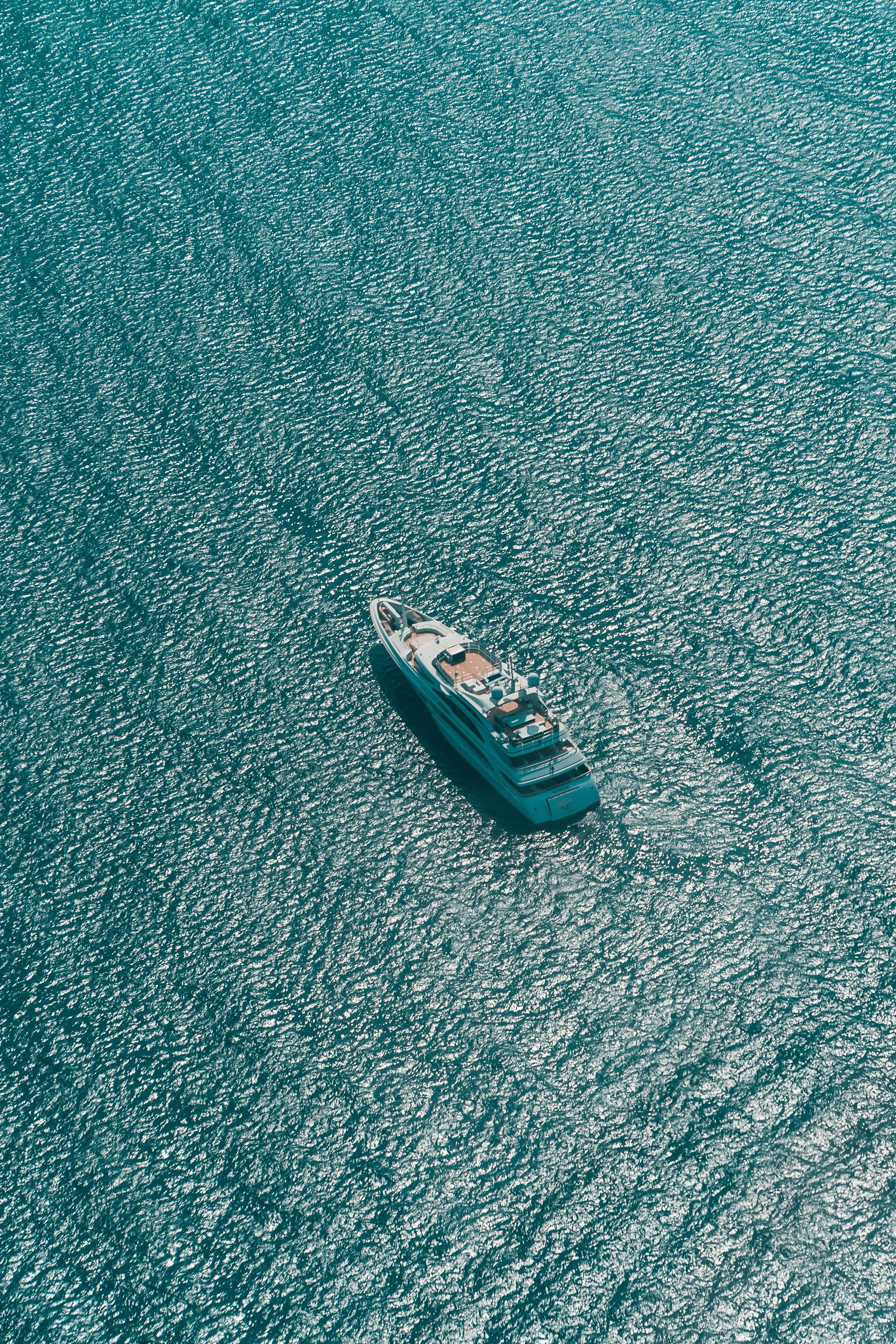 An aerial view of a large yacht sailing on a calm, turquoise sea, with shimmering water.
