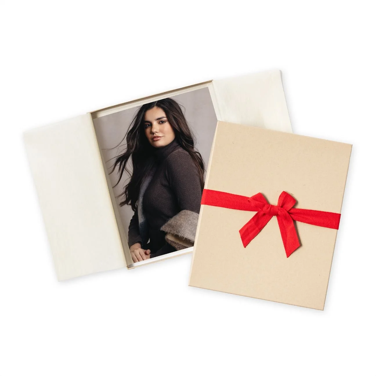 A framed portrait of a woman with long dark hair, wearing a dark sweater, next to a beige gift box wrapped with a red ribbon and bow.