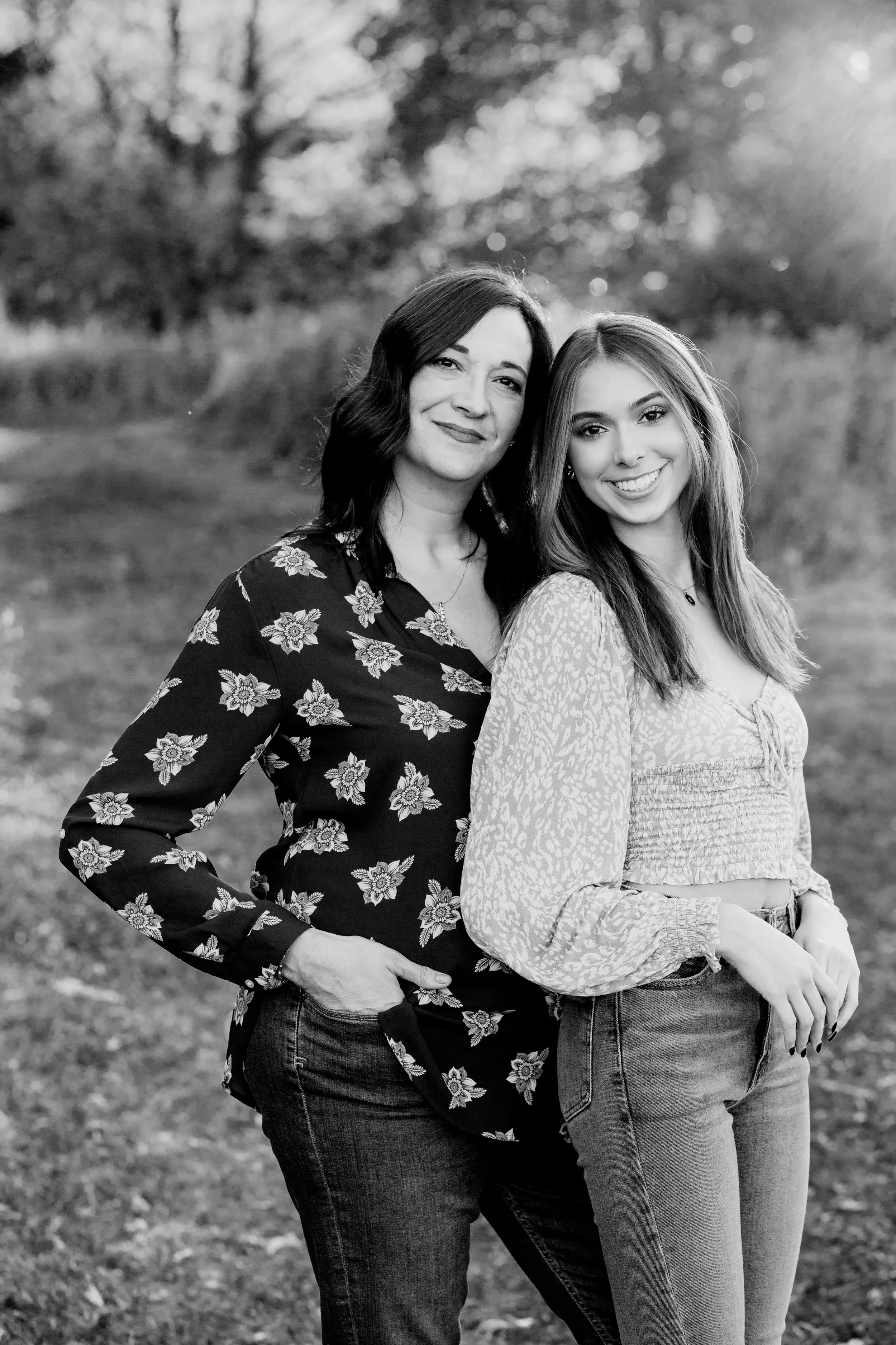 Two women standing outdoors in a park on a sunny day, smiling at the camera.