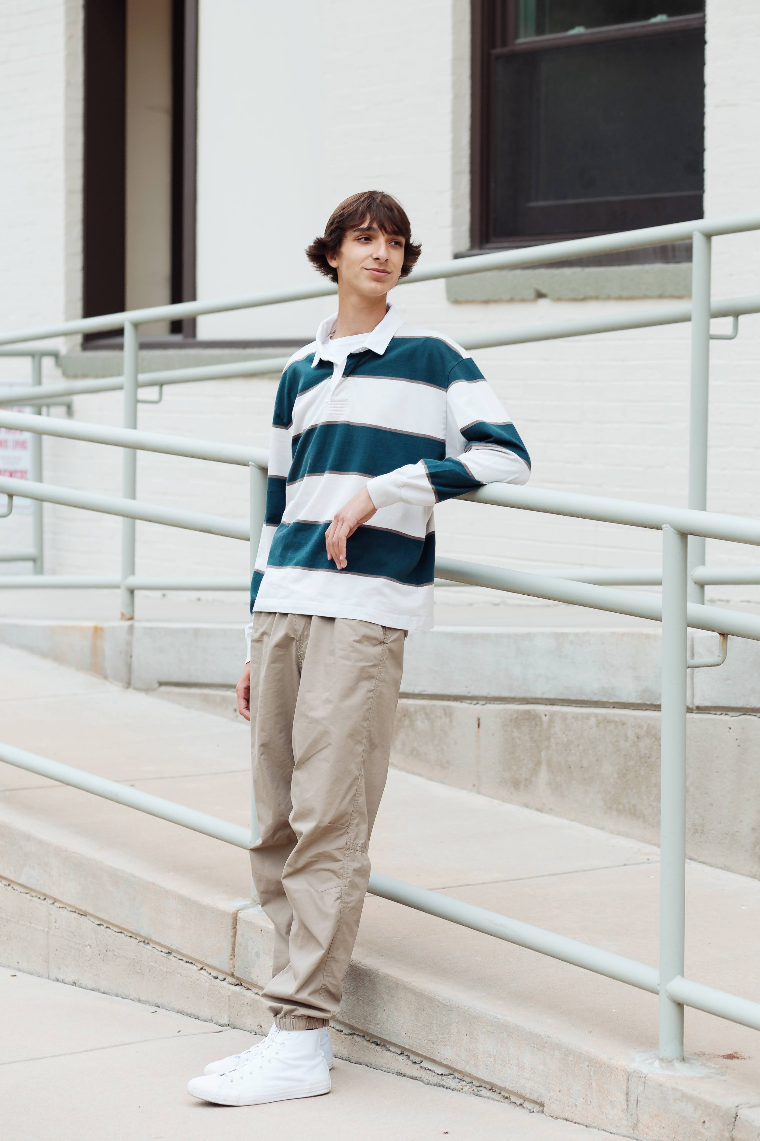 Teen boy in a striped shirt leaning against a railing during a senior portrait session in Raleigh, NC