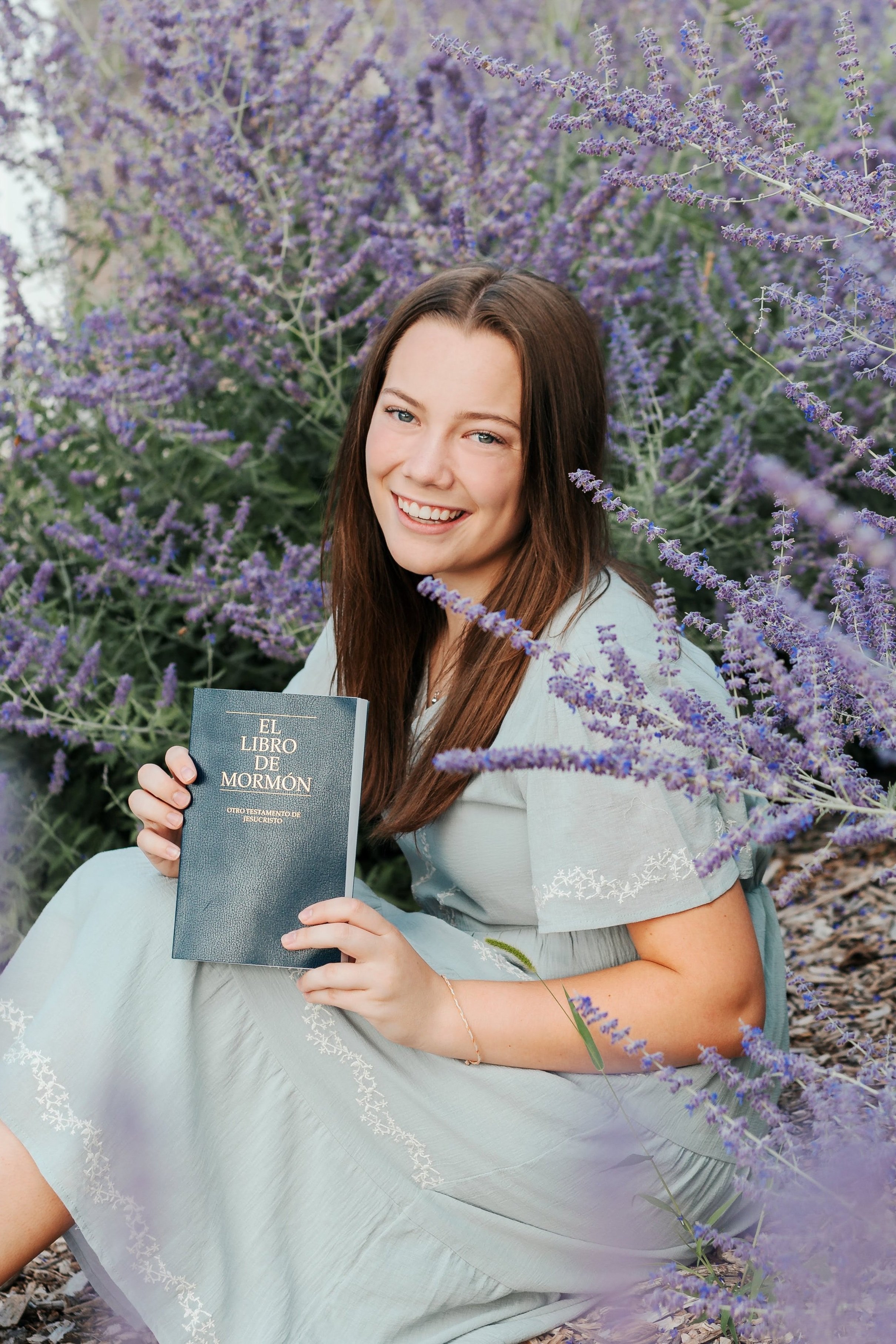 Smiling senior girl holding a book while sitting among purple lavender during a senior portrait session in Wake Forest, NC
