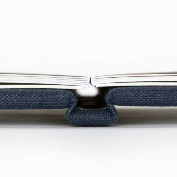 Close-up of a notebook with a fabric cover, open with visible spine, placed on a white surface.