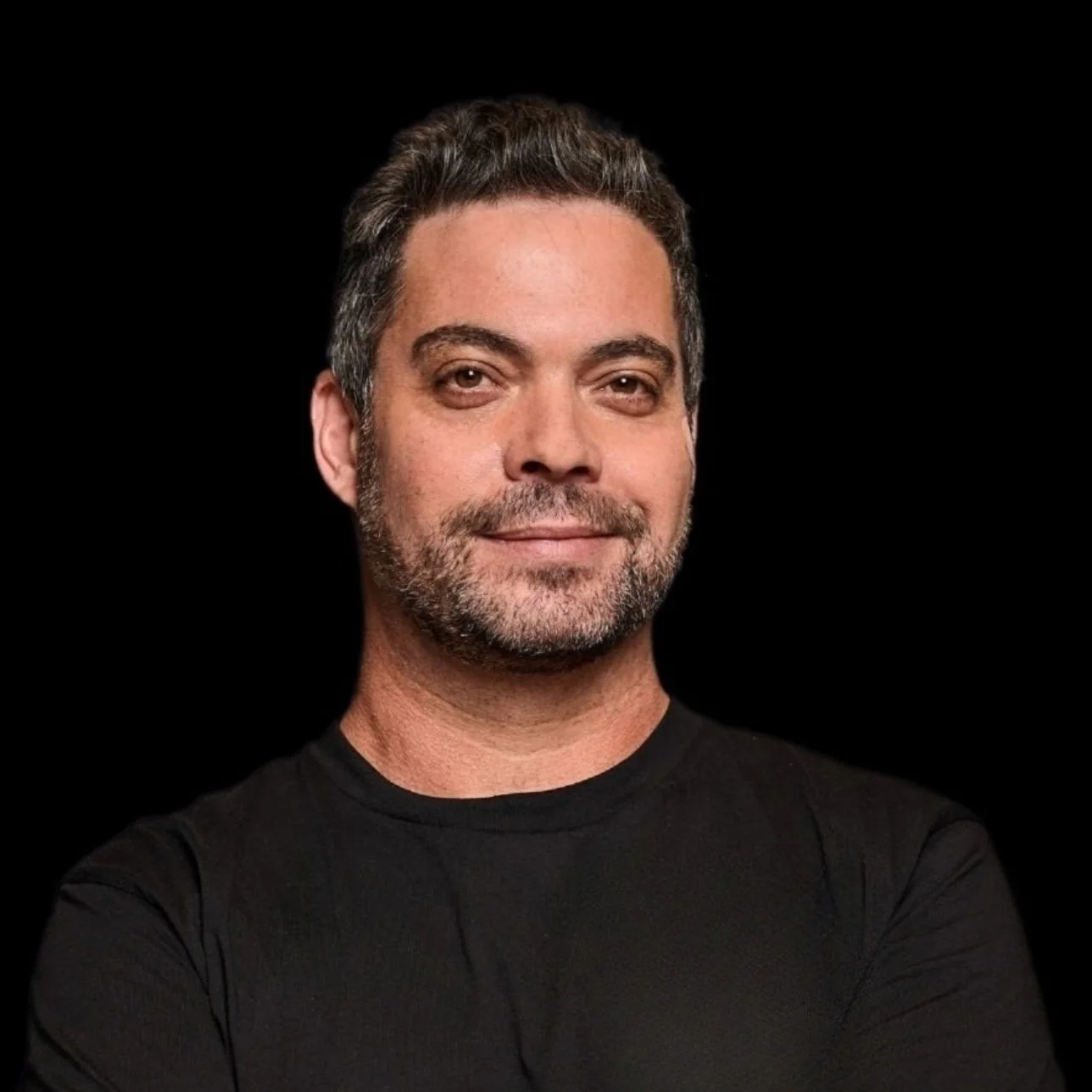 Man with dark hair and beard smiling against black background