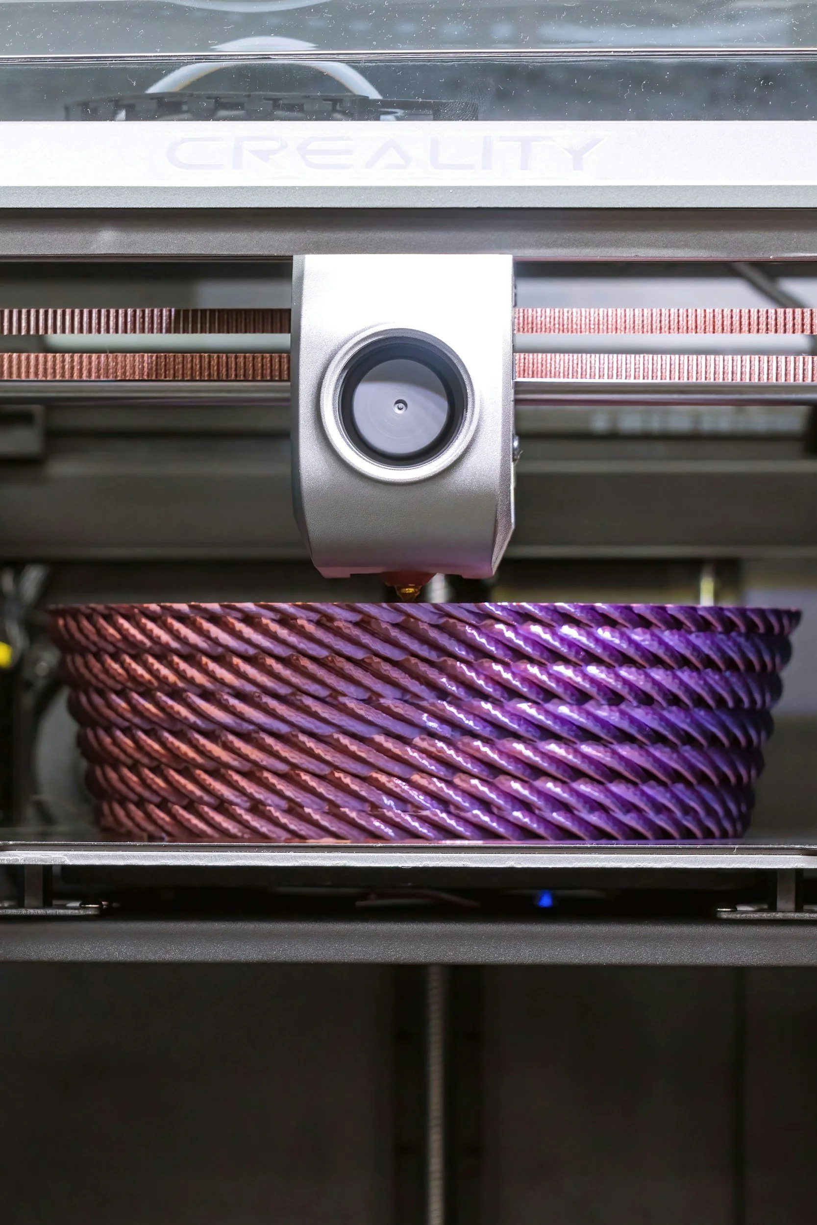 A 3D printer creating a purple and pink twisted filament object.