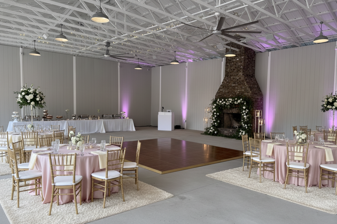 Wedding reception setup in an industrial-style hall with decorated tables, a dance floor, and a brick fireplace adorned with flowers.