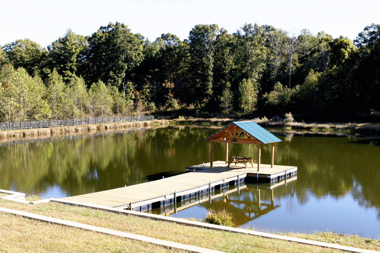 A small dock with a gazebo and picnic table on a calm pond, surrounded by trees.
