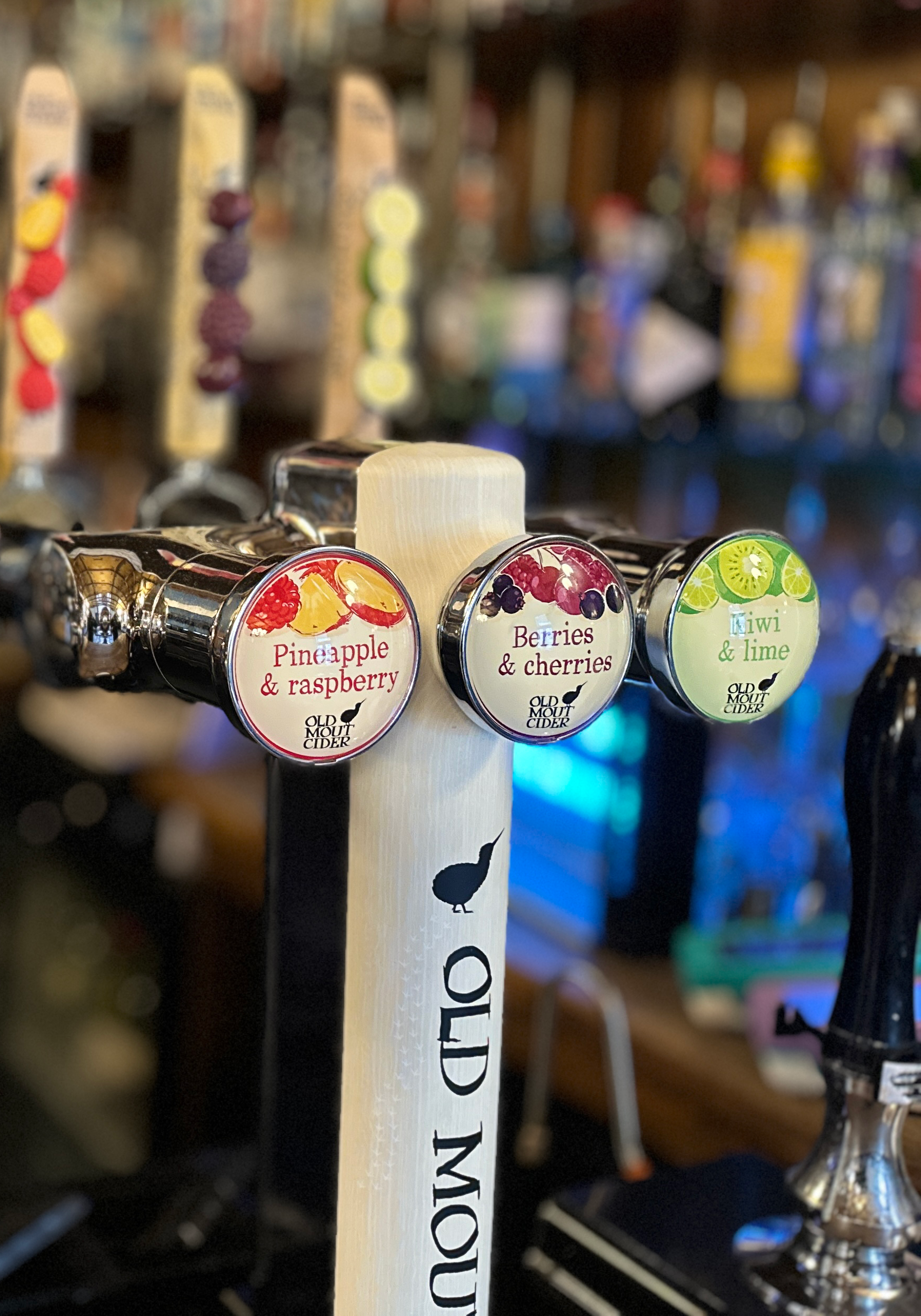 Beer tap handles labeled with fruit flavors: pineapple & raspberry, berries & cherries, kiwi & lime at Old Mout Cider bar.