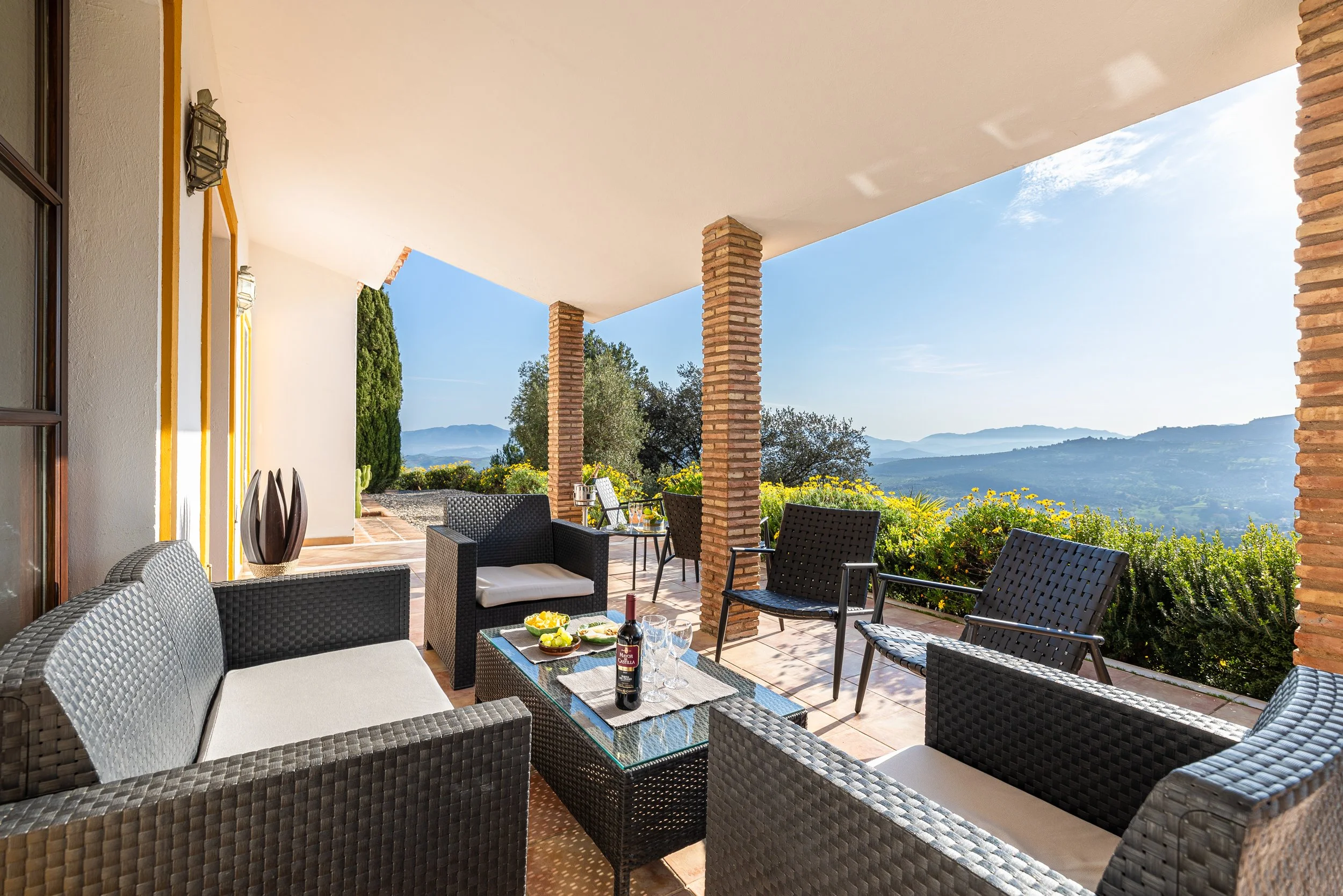 Outdoor patio with wicker furniture, a glass table, and a scenic mountain view in the background.