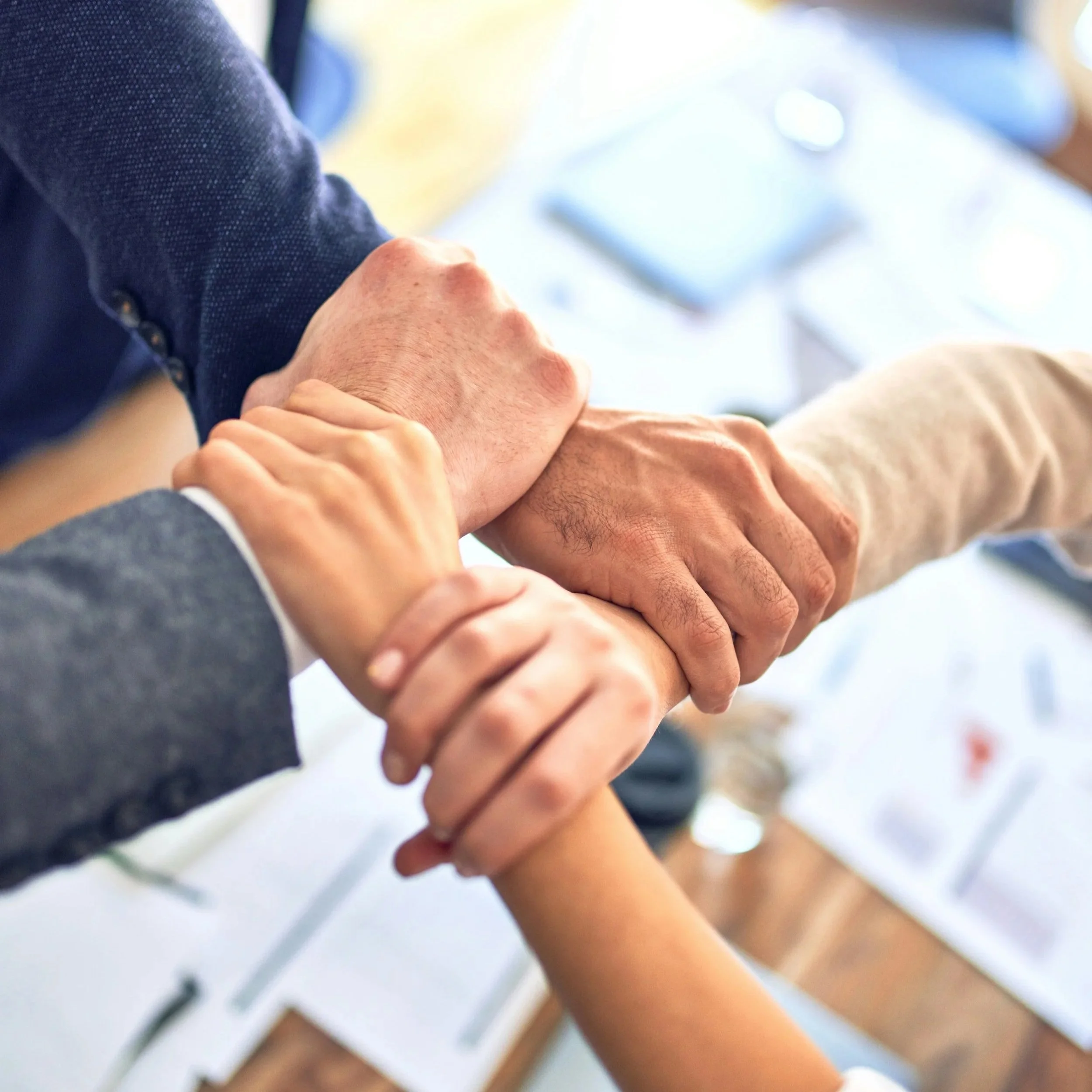 Multiple hands joined together in a display of unity during a meeting.
