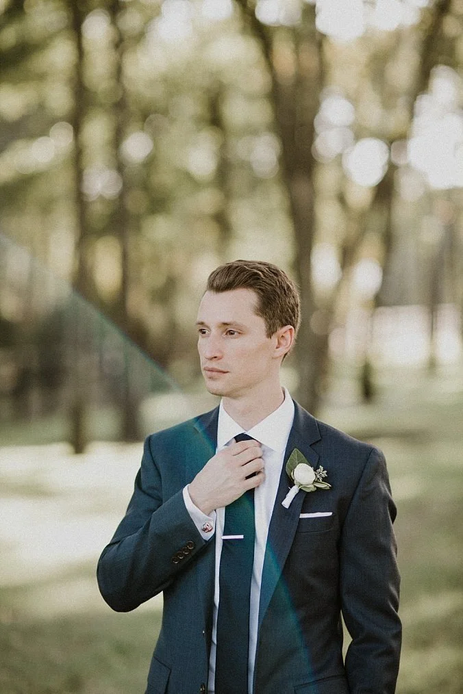Groom wearing a white ranunculus and black tie with a tie clip at this outdoor wedding