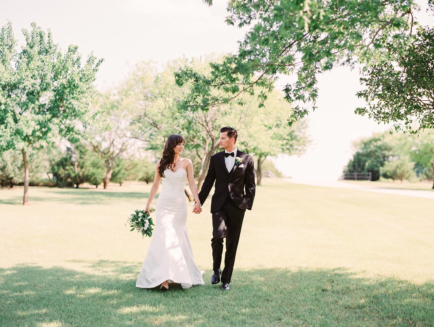 Bride and groom walking outside and big open field in classic wedding attire at Milestone in Denton