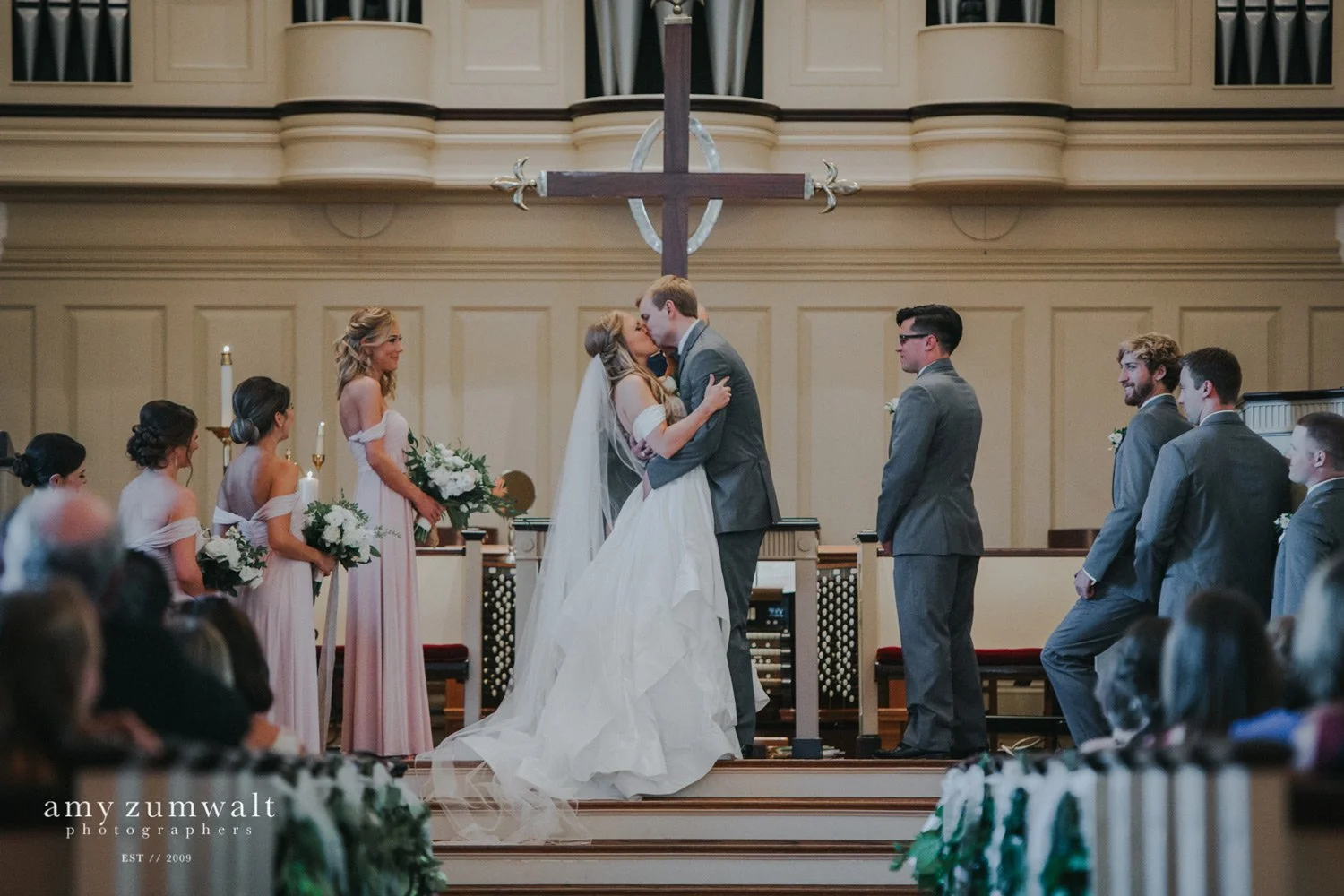 Bride and groom first kiss in front of cross