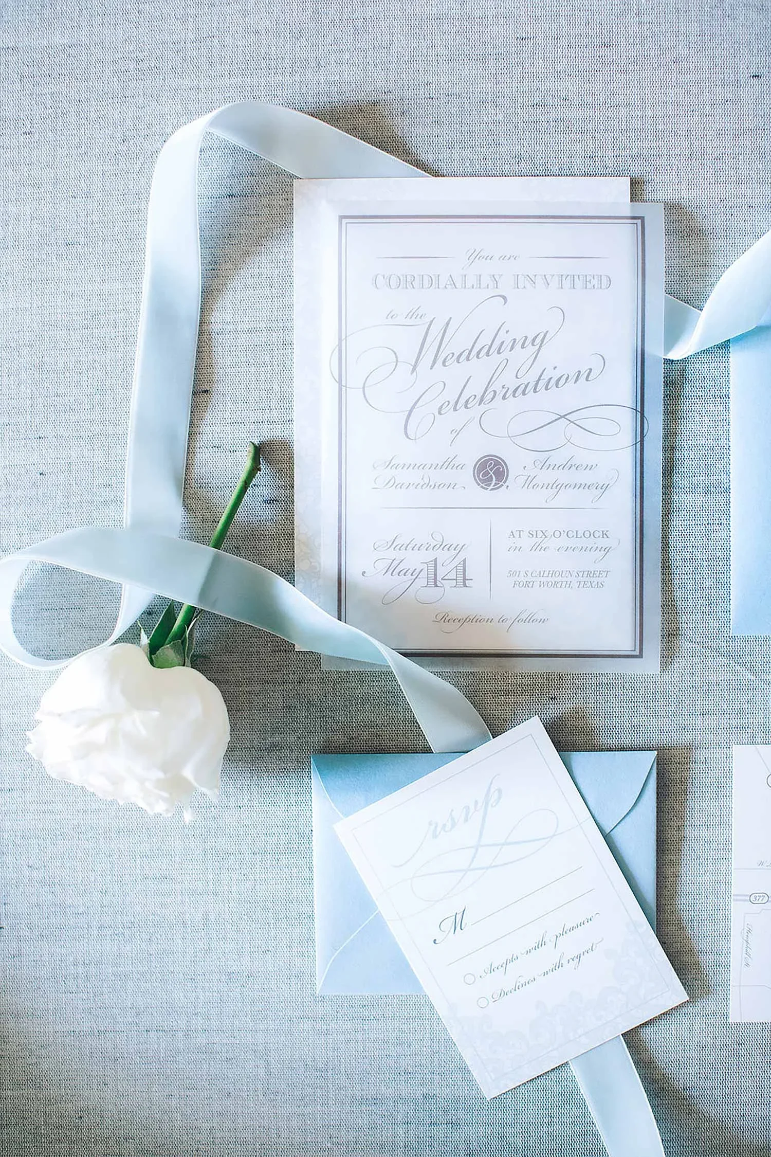 Acrylic wedding invitation and dusty blue envelope with a white rose