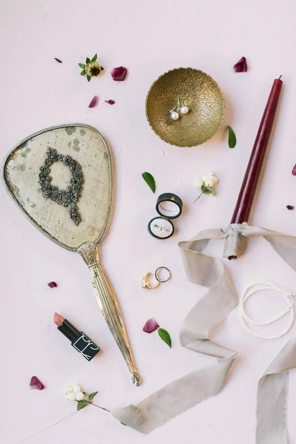 Bridal flat lay with a vintage mirror, lipstick, and a red tapered candle