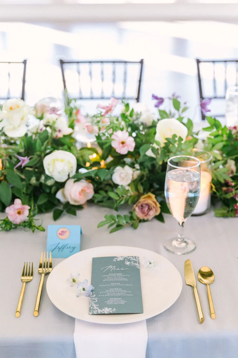 Navy blue menu on a white plate with a loose pink and purple floral garland at Dove Ridge Vineyard