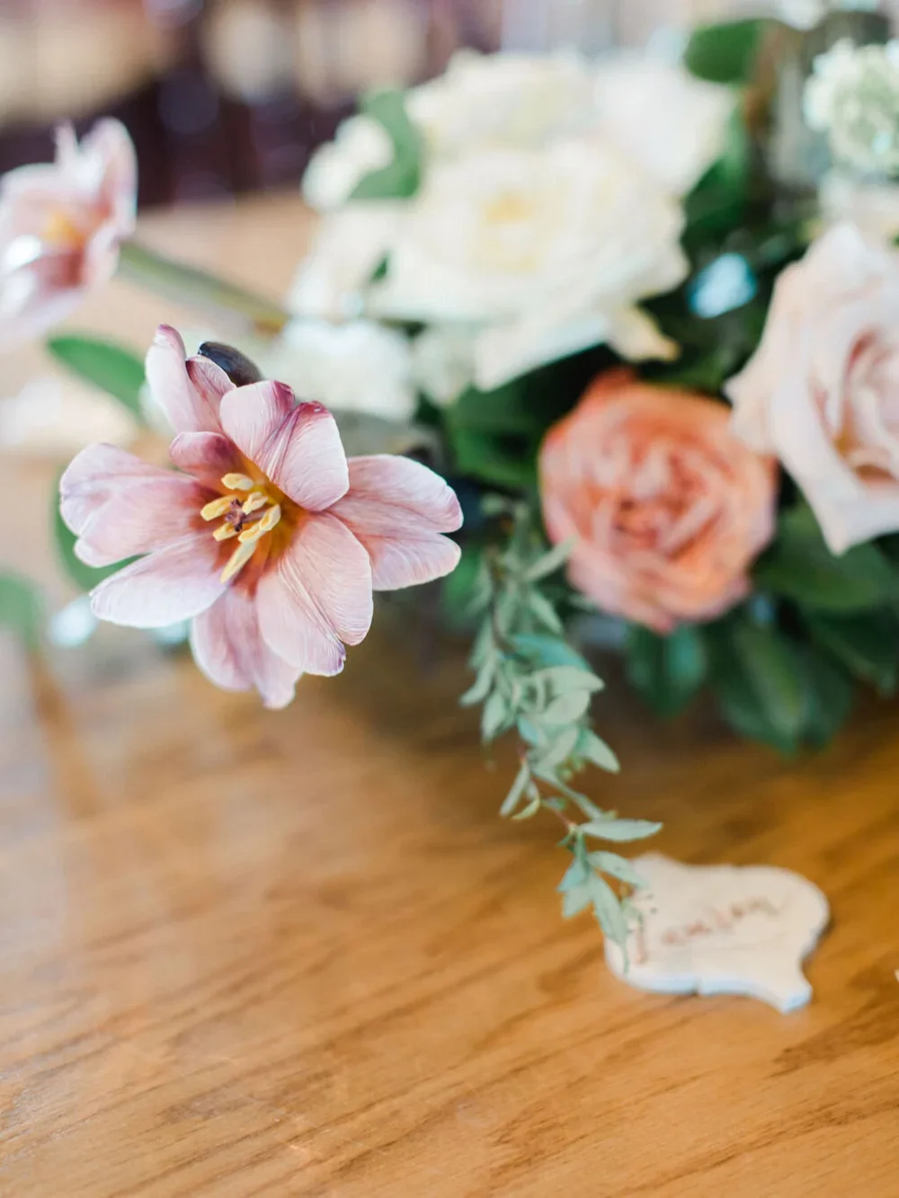 White arabesque escort card on wood table with pink flowers