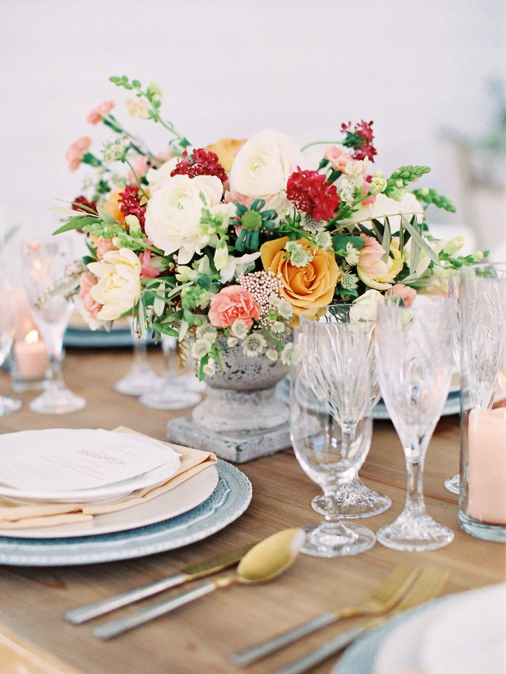 Red Orange &amp; Pink flower arrangement on farm table with blue charger