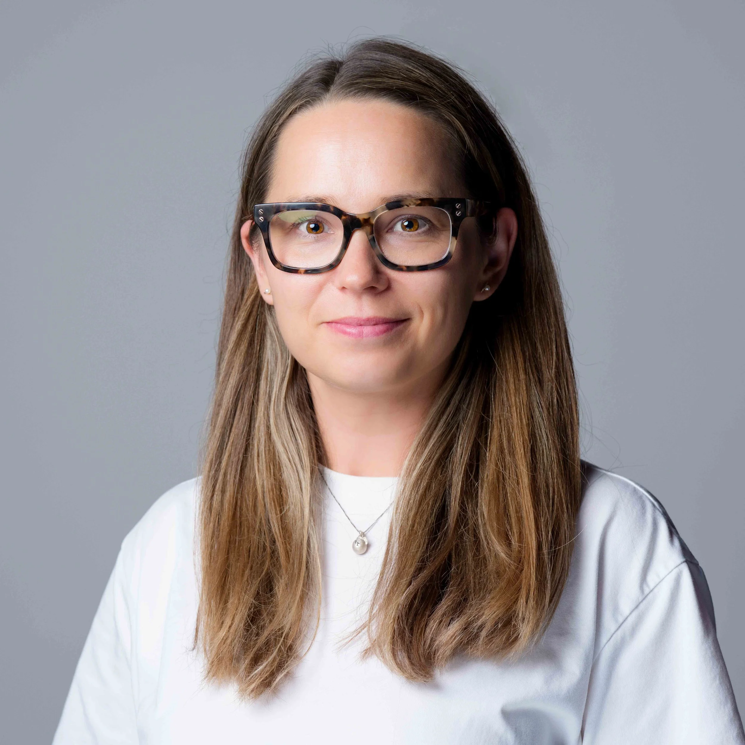 Professional headshot and branding photography of a woman smiling while seated at a table with a laptop and smartphone in a modern living room setting.