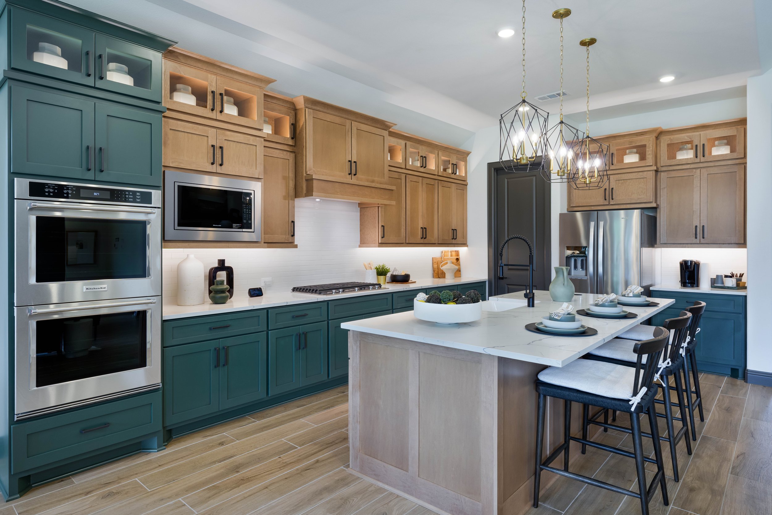 A modern kitchen photographed for a real estate listing, featuring blue and wood cabinetry, stainless steel appliances, a white marble island, and decorative pendant lighting.