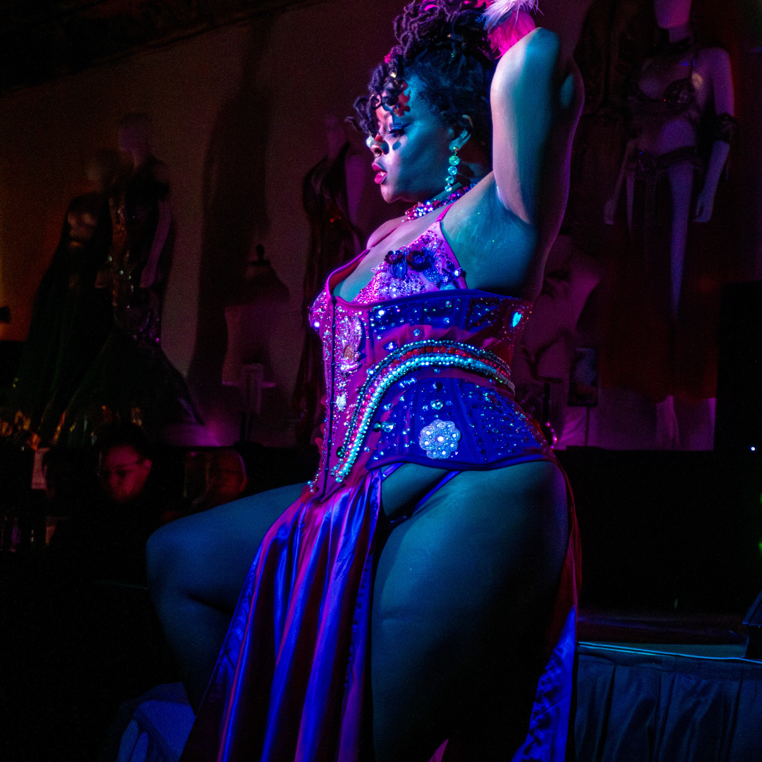 A woman in a revealing, sequined costume performing in a nightclub with colorful lighting.