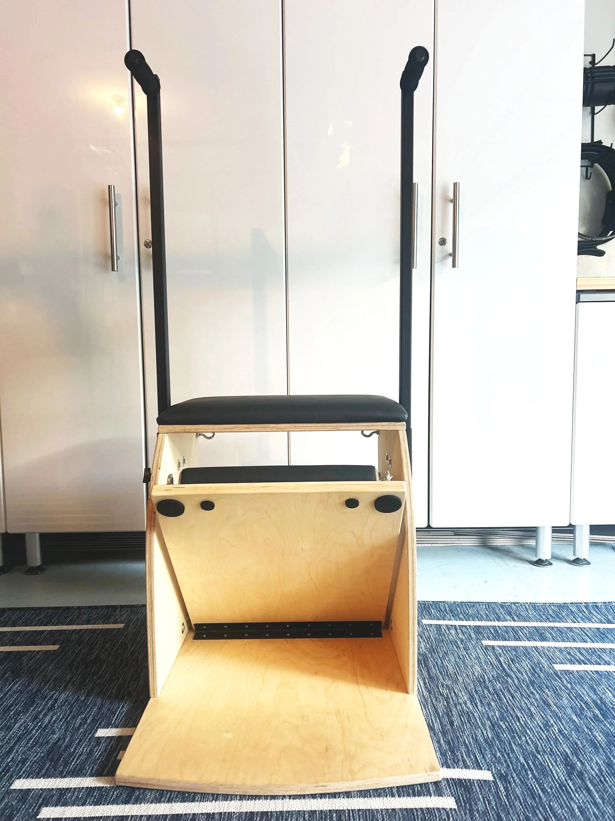 A workout step platform with two black handles attached, positioned in front of white cabinets in a room.