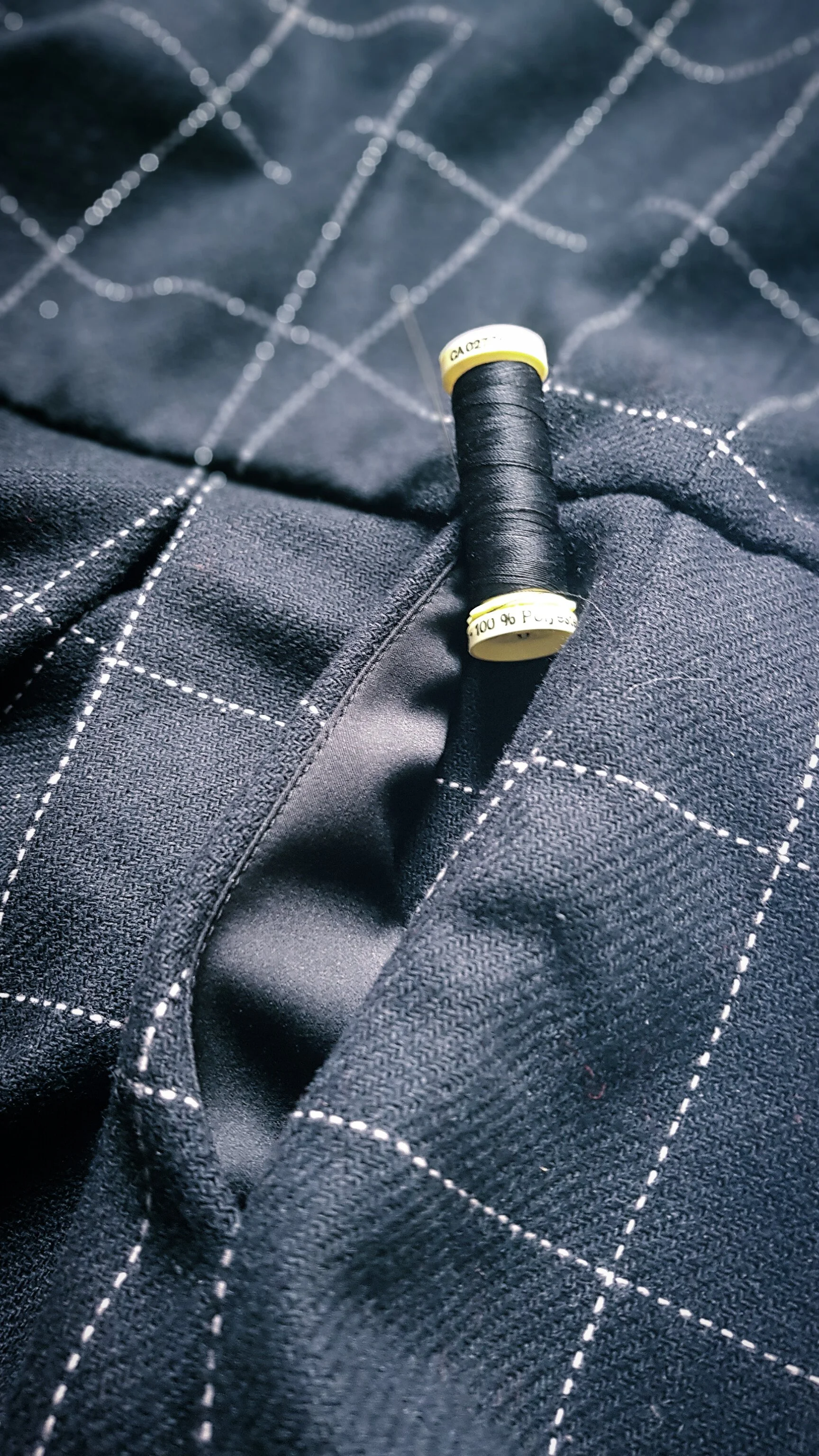 Un assortiment de fil à couture noir avec une bobine posée sur du tissu noir à motifs à carreaux blancs.