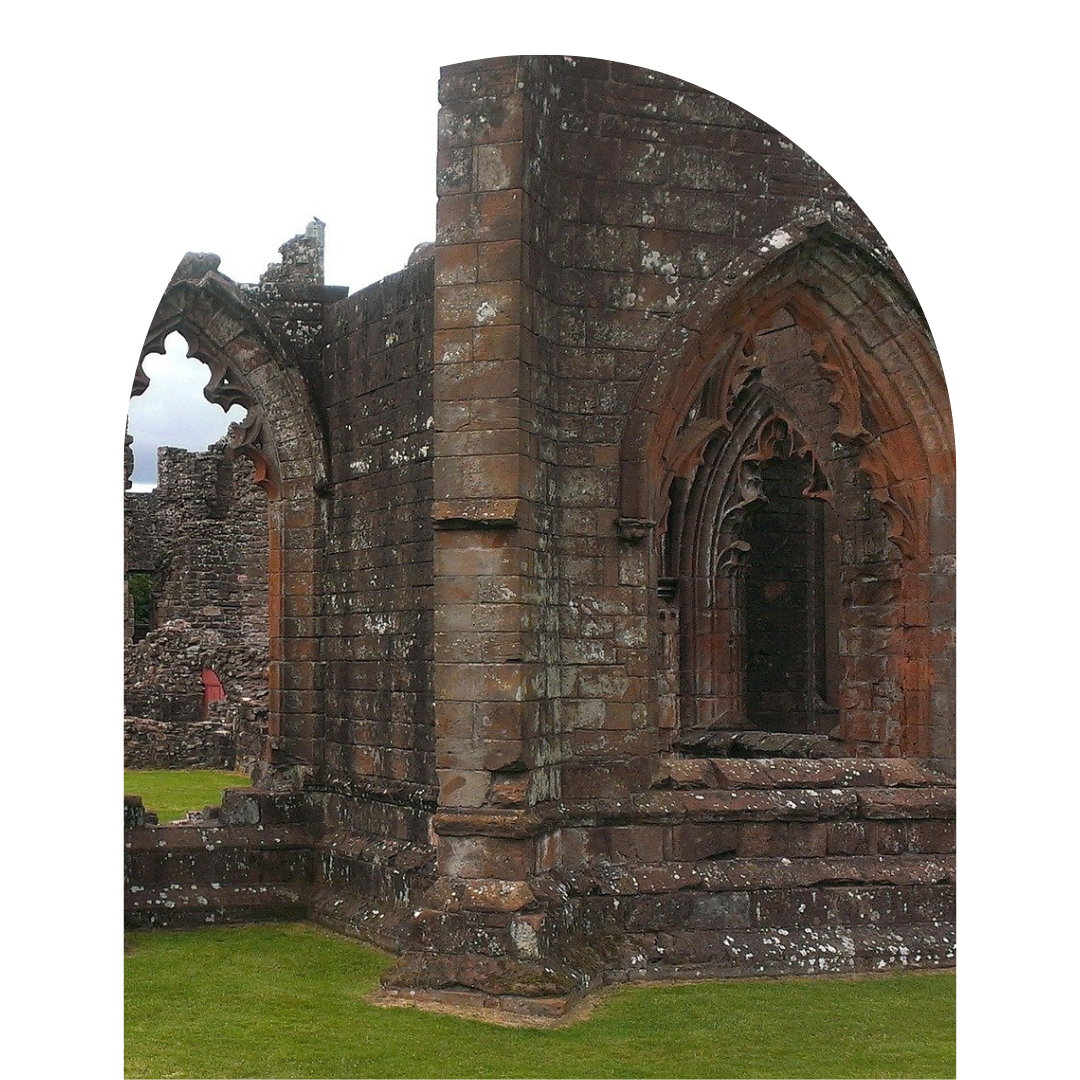 Ancient stone ruins of a Gothic-style building with arched windows and intricate detailing, surrounded by green grass.