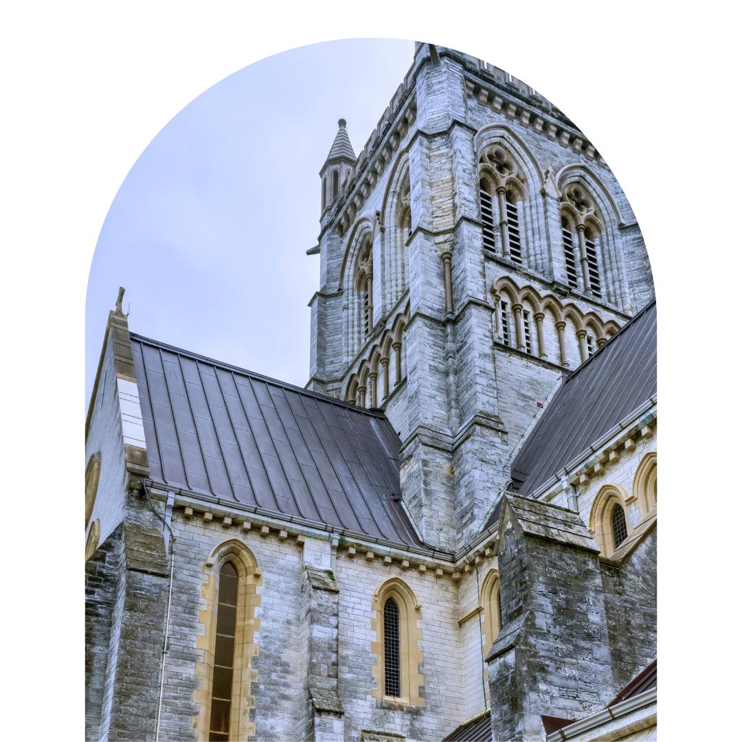 A close-up view of a historic stone church with arched windows and a tall steeple, viewed from below.