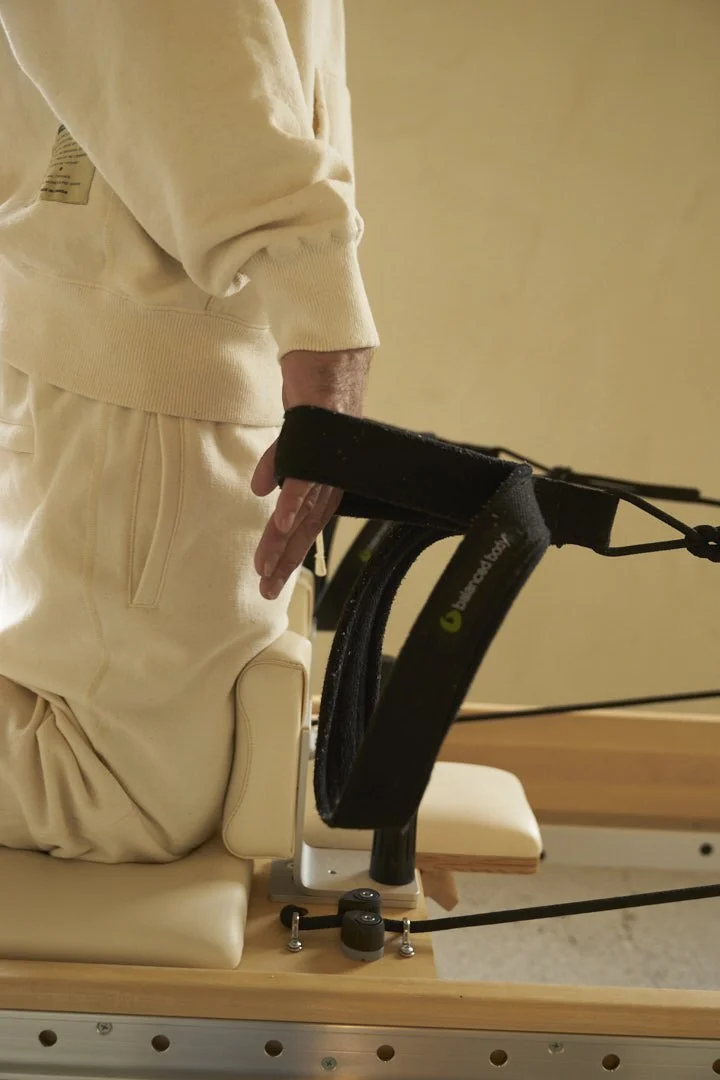 Person kneeling on a padded surface using a specialized lifting device with straps and a hydraulic or pneumatic system