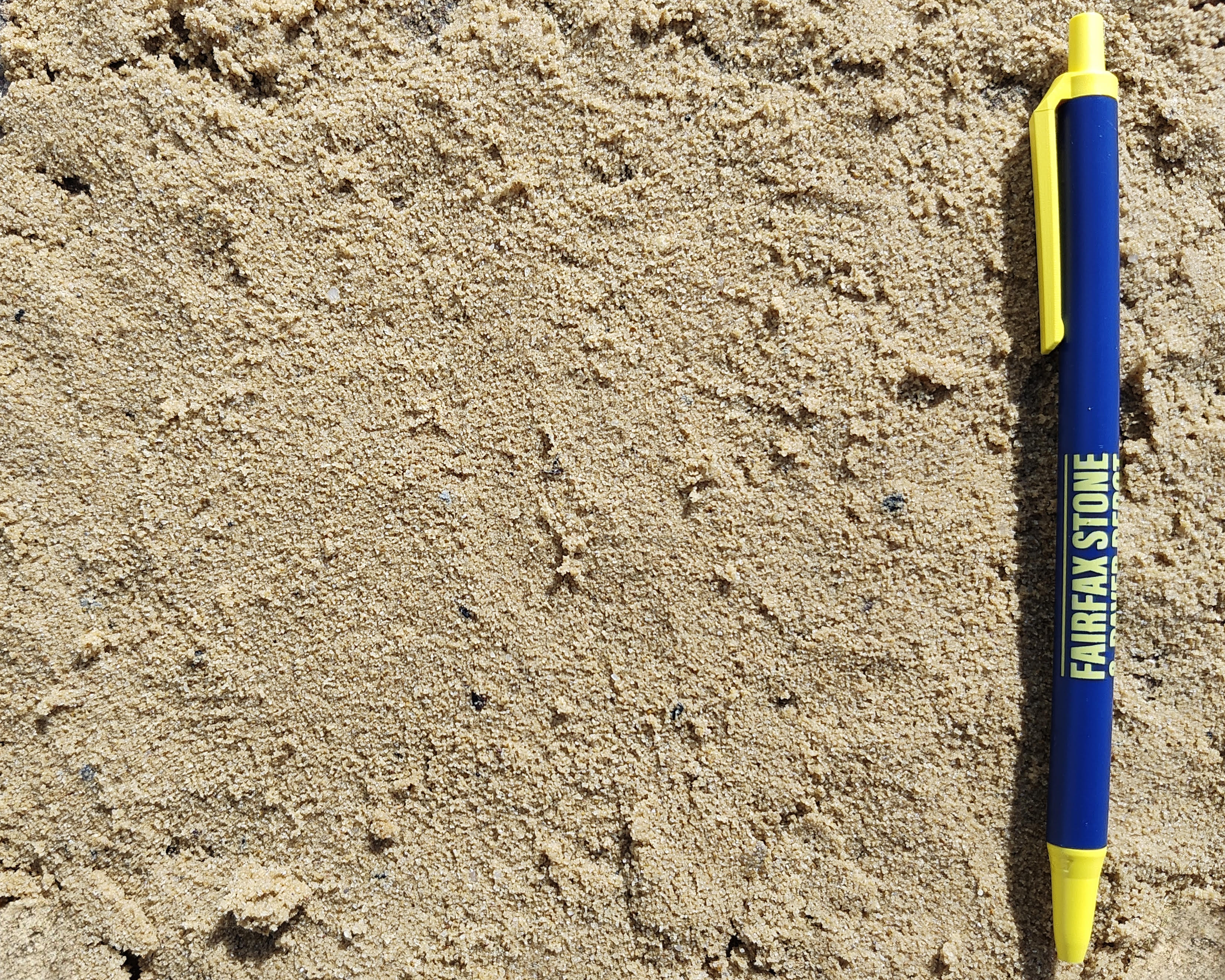 A blue and yellow pen lying on fine masonry sand near the right edge of the image.
