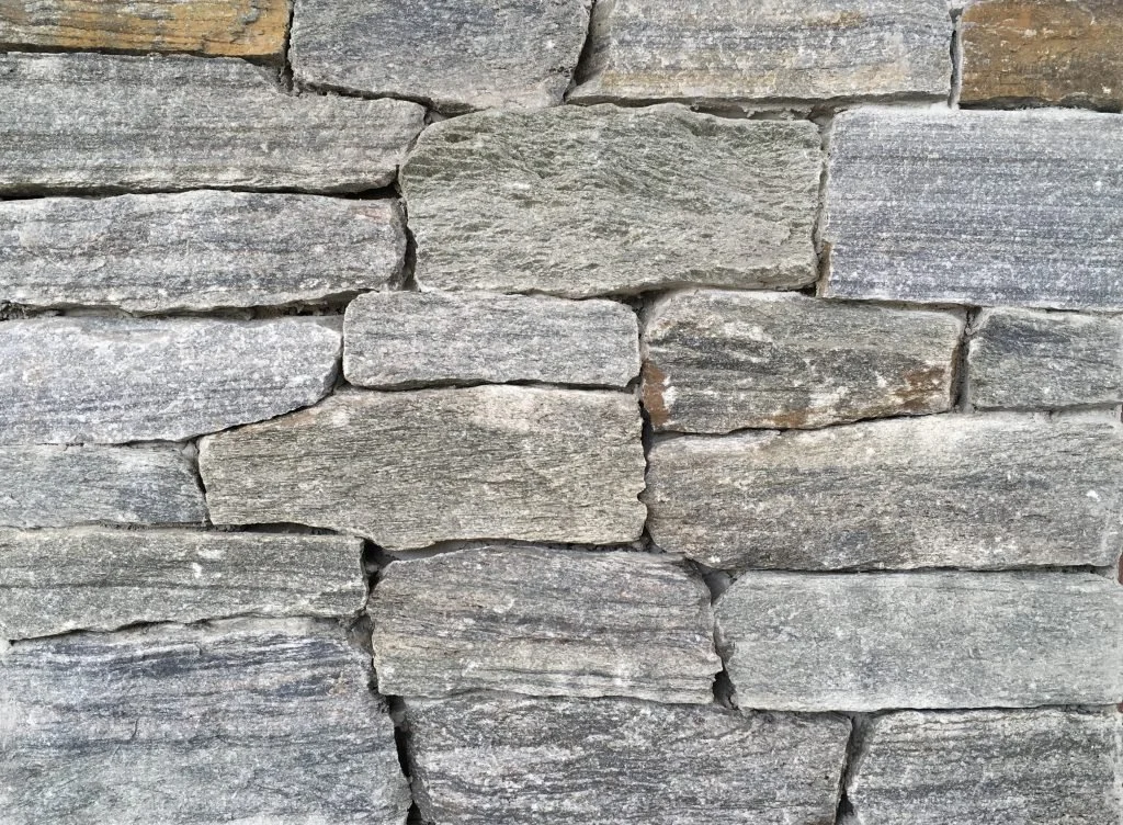 Close-up of a stone wall made of stacked, uneven gray limestone rocks.