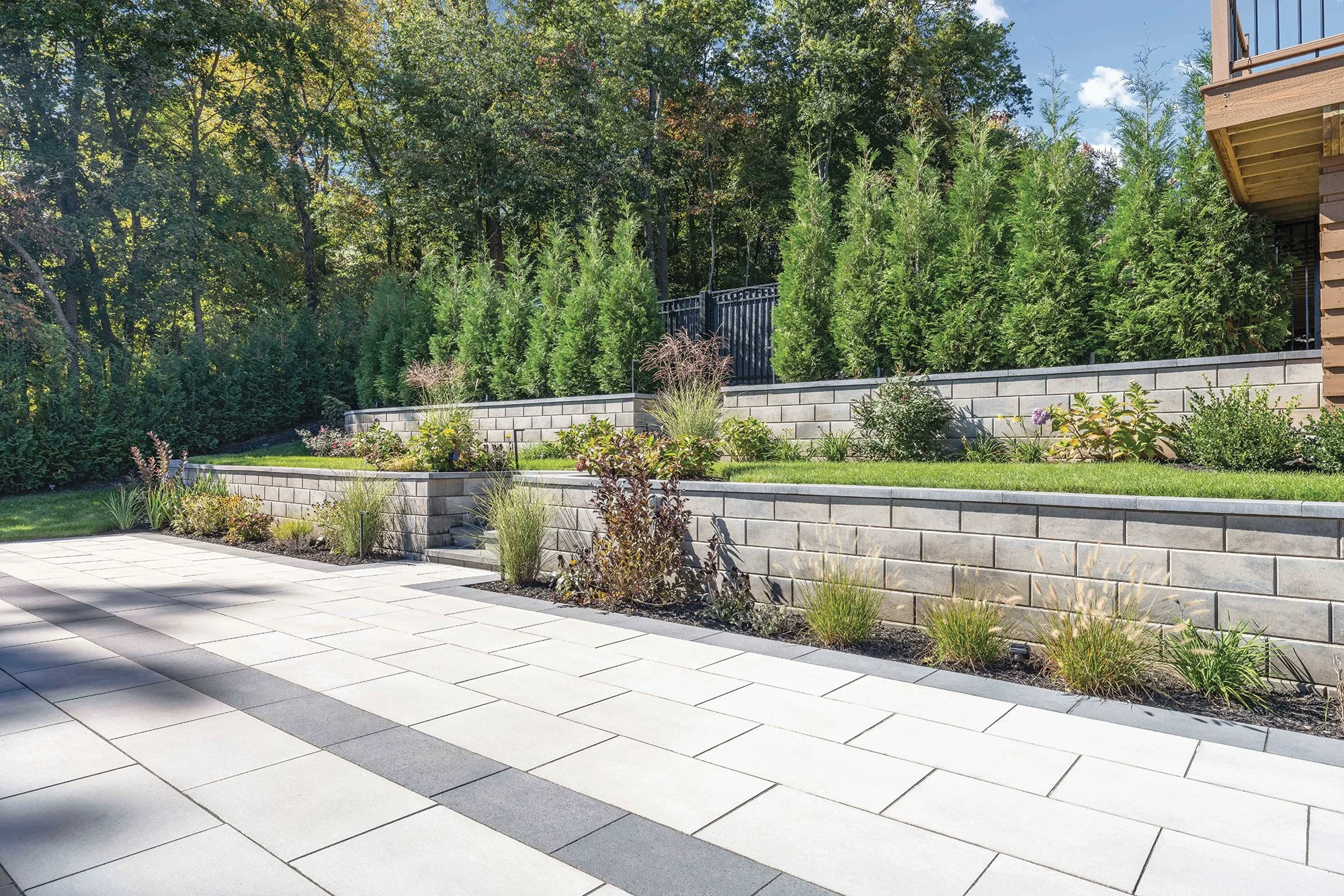 Two tiered retaining wall with plantings, over a large format concrete paver patio with a linear, running bond pattern.