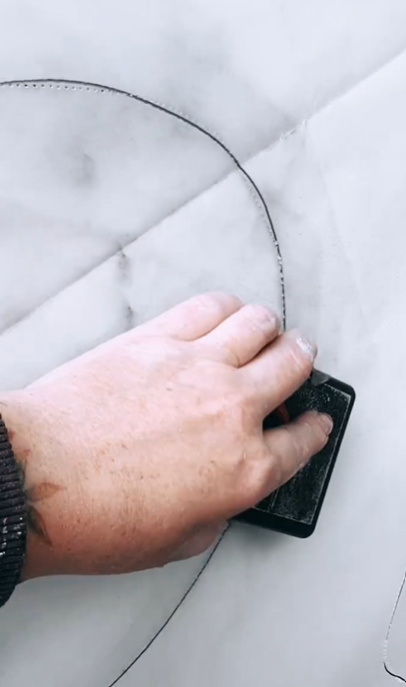 A hand holding a rotary cutter is cutting a piece of fabric along a curved line.