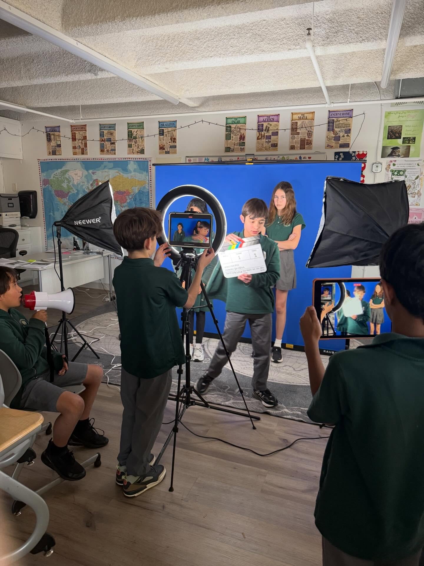Lights, camera, action! 🎬 In our afterschool Digital Media program, students film, direct, and edit their own projects and this is a snapshot of them filming a comedy news story on a blue screen.